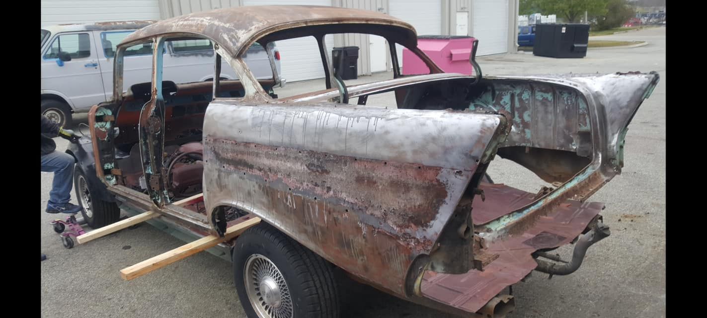 A rusty old car is sitting on a trailer in a parking lot.