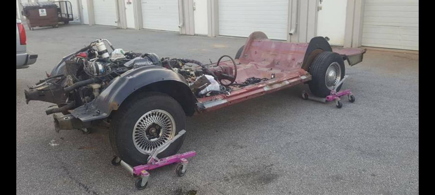 The chassis of a car is sitting on wheels in a parking lot.