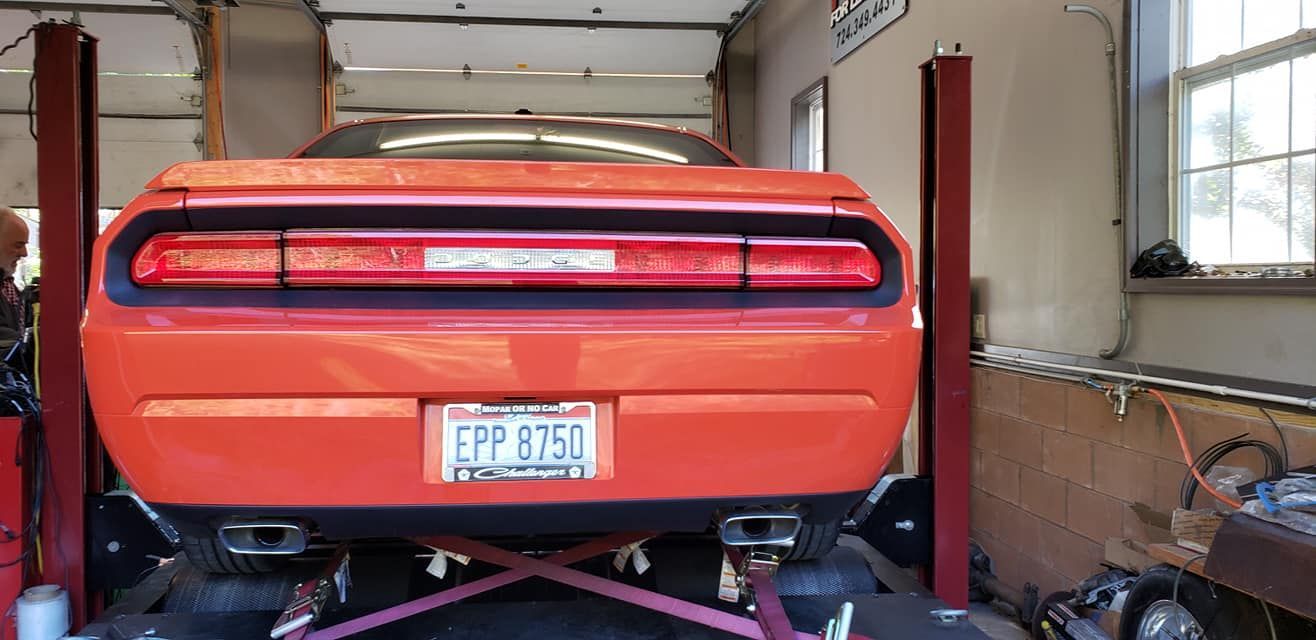 An orange dodge challenger is on a lift in a garage.