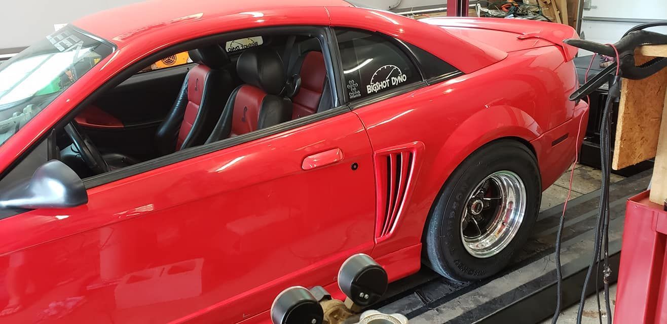 A red mustang is sitting on a ramp in a garage.