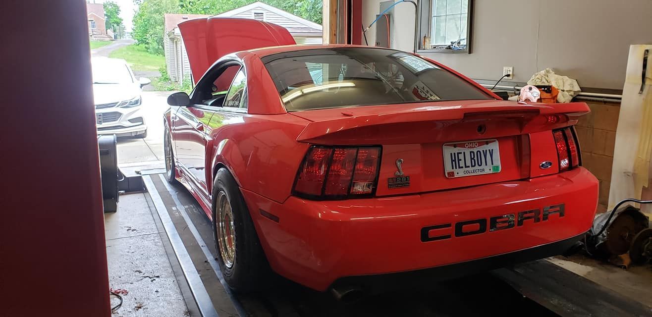 A red mustang is parked in a garage with the hood up.