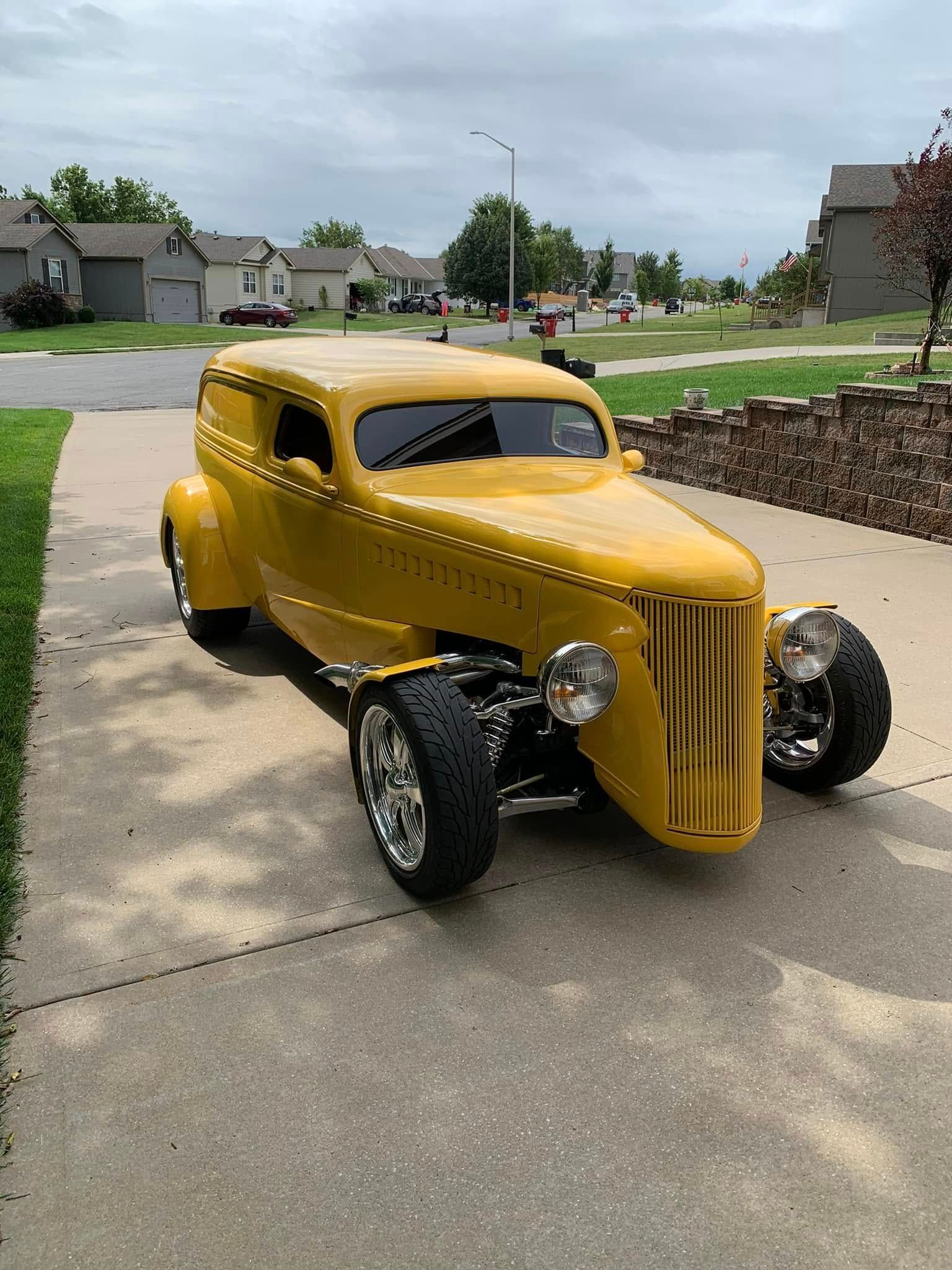 A yellow car is parked on the side of the road in a driveway.