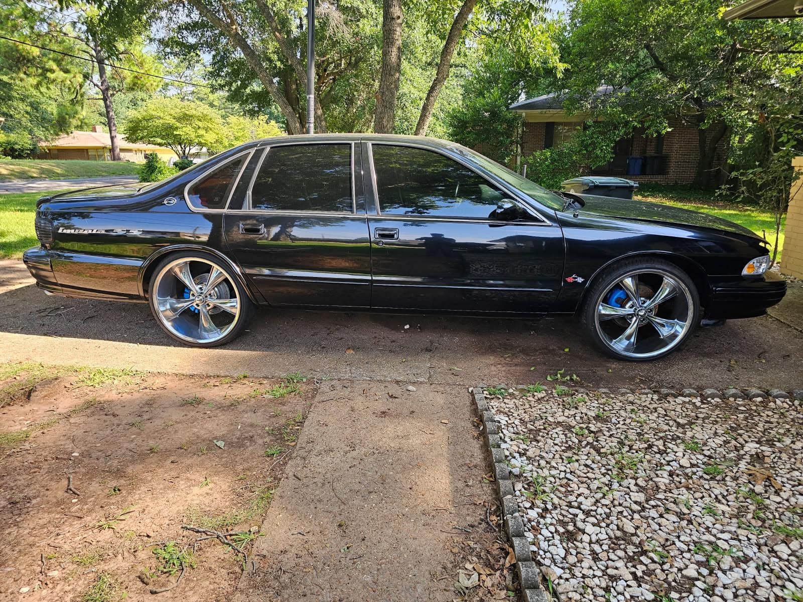 A black car is parked on the side of the road in a driveway.