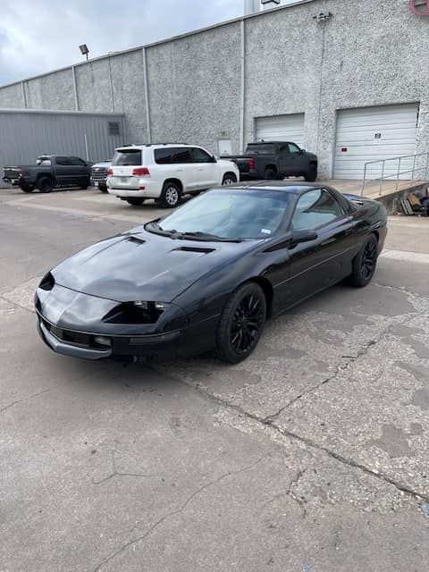 A black car is parked in a parking lot in front of a building.