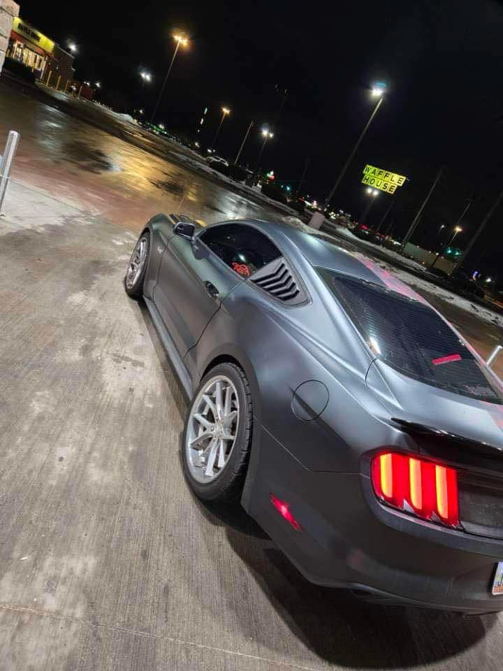 A black mustang is parked in a parking lot at night.