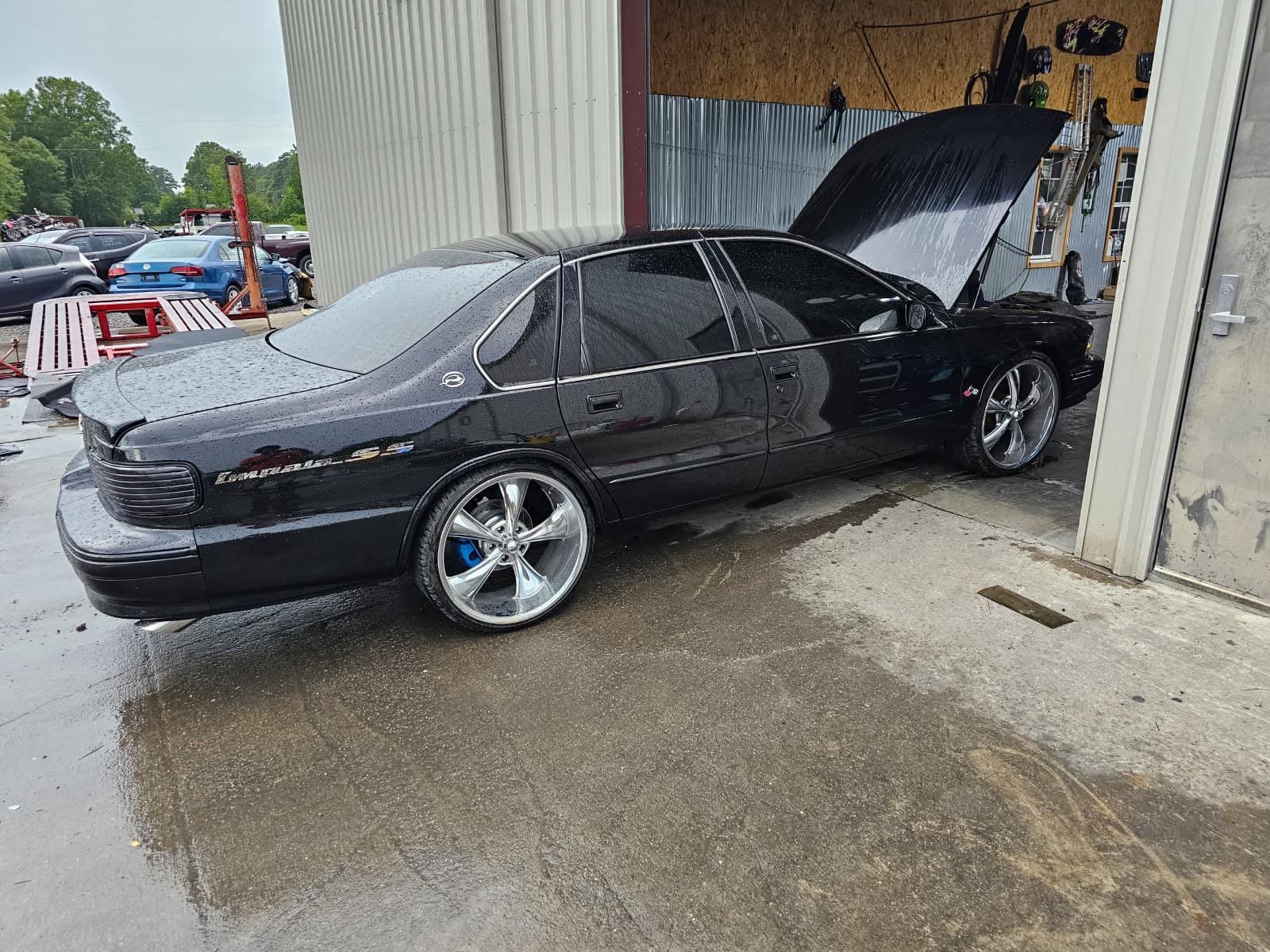 A black car with the hood up is parked in front of a garage.