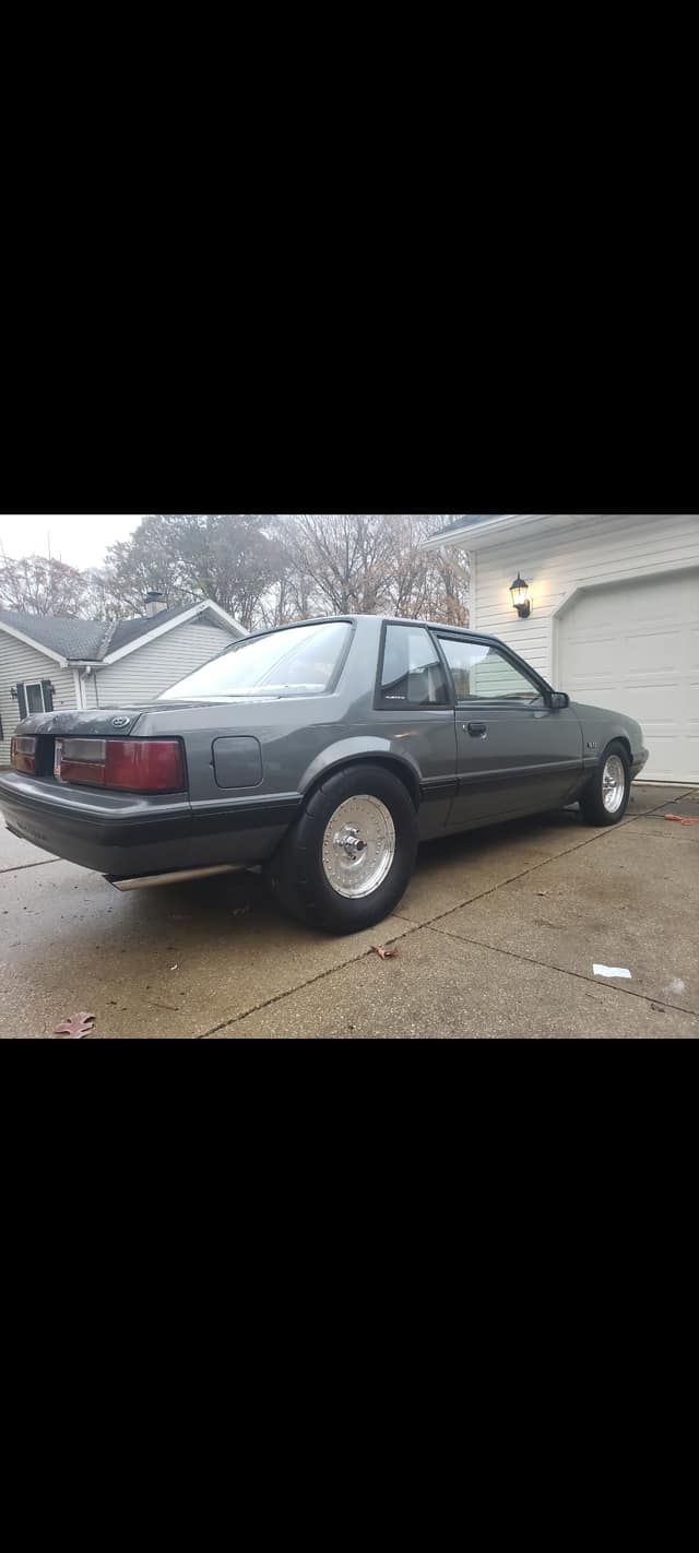 A gray mustang is parked in a driveway next to a garage.