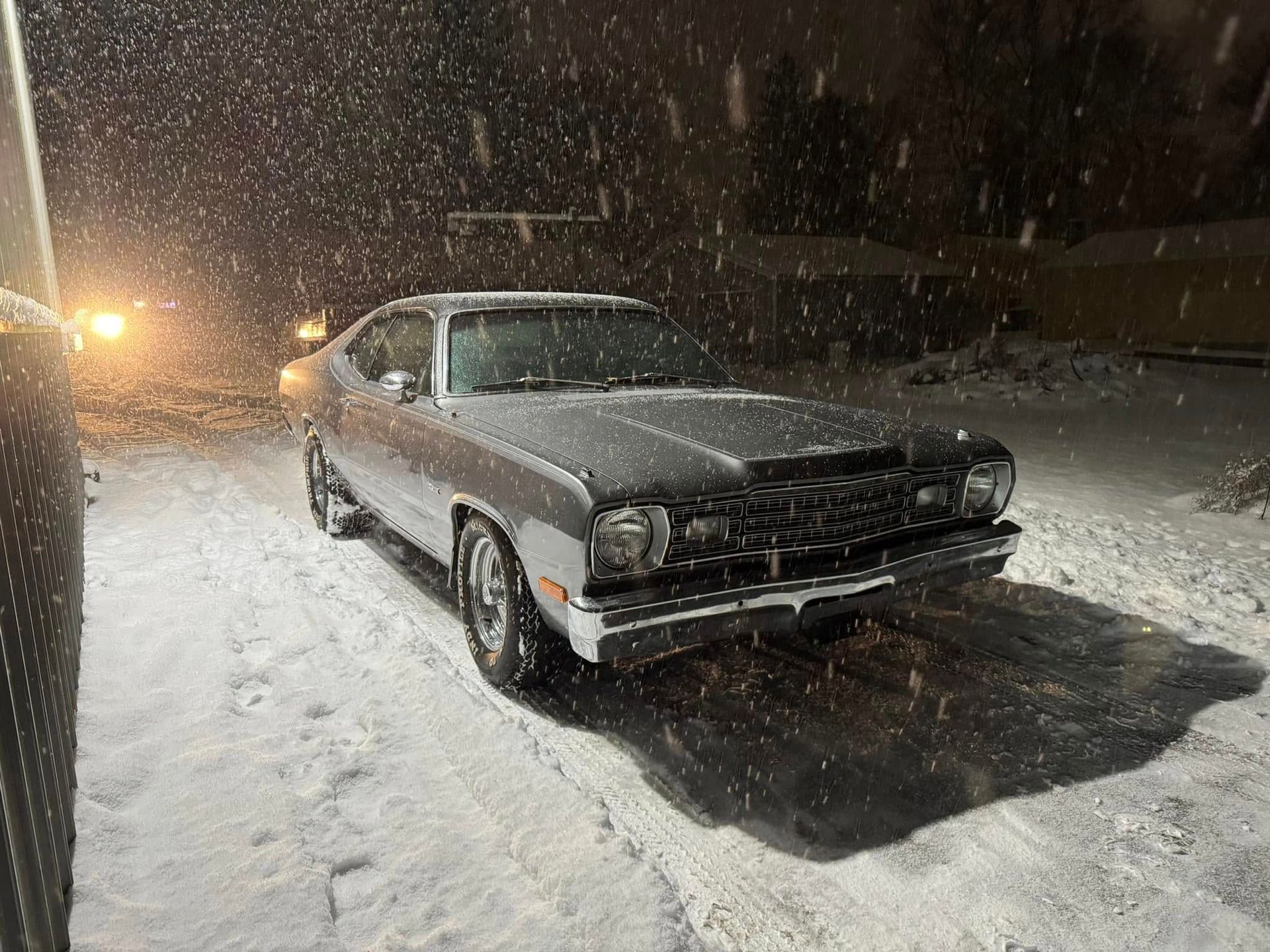 A silver car is parked in the snow at night.