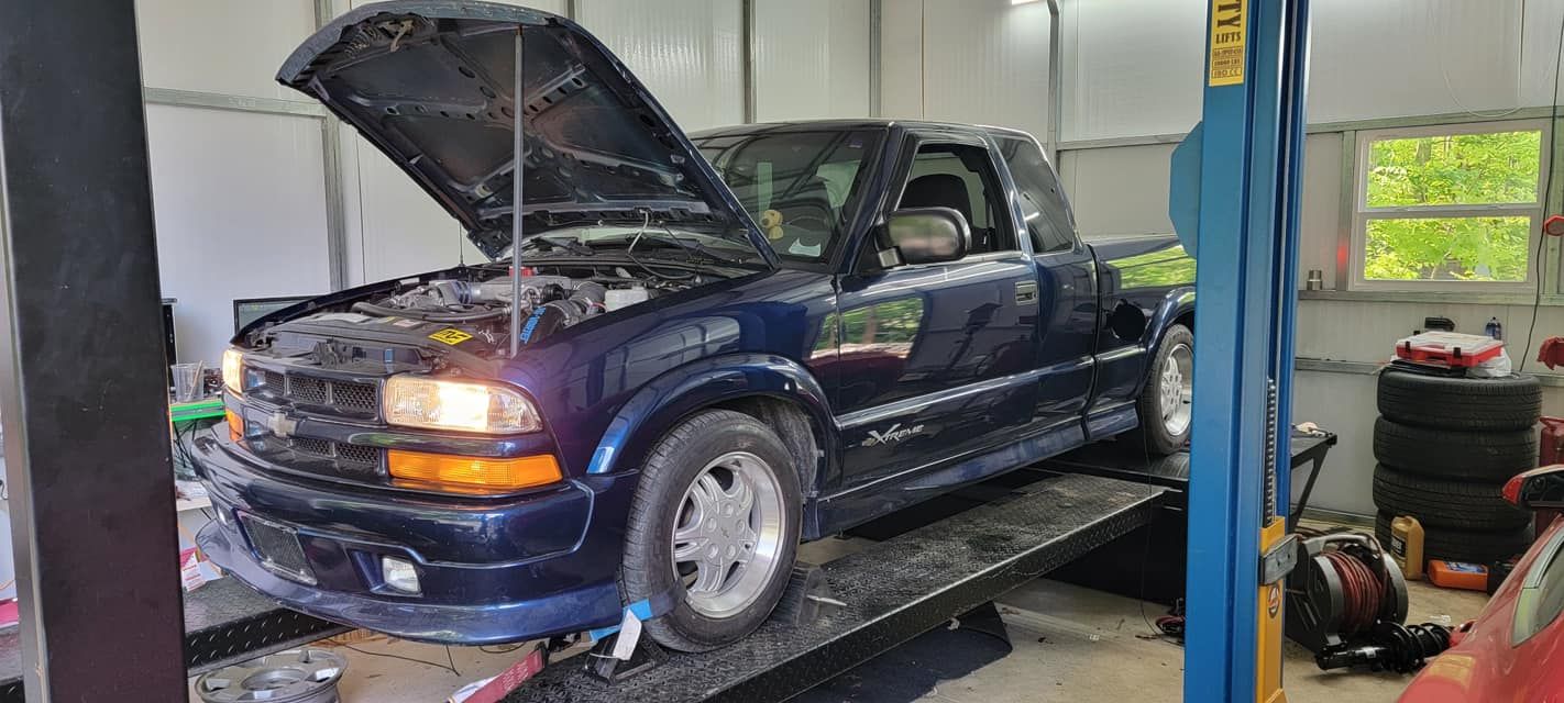 A blue truck with the hood up is sitting on top of a tow truck.