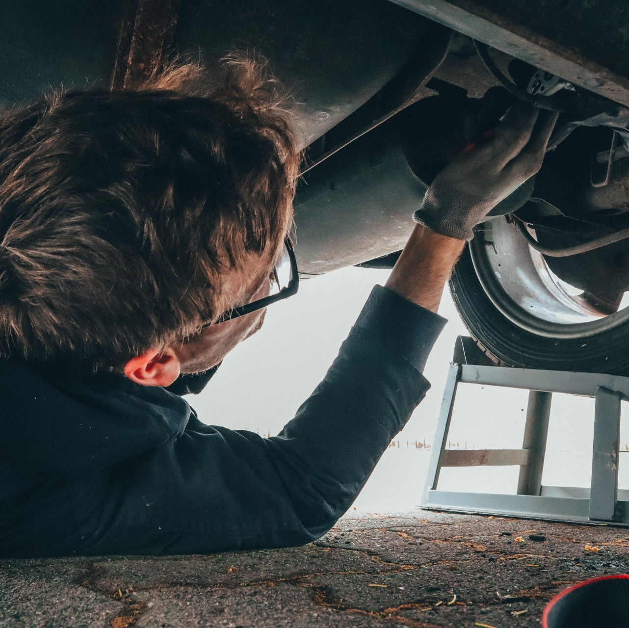 A man wearing glasses is working under a car