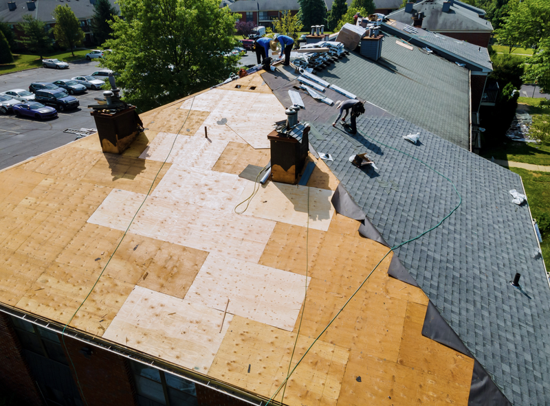 Roofers replacing shingles on a building with chimneys. Some roof is exposed plywood.