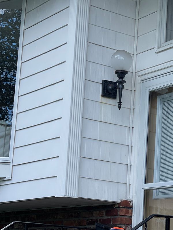 White siding on a house with a black wall light fixture and a globe bulb.