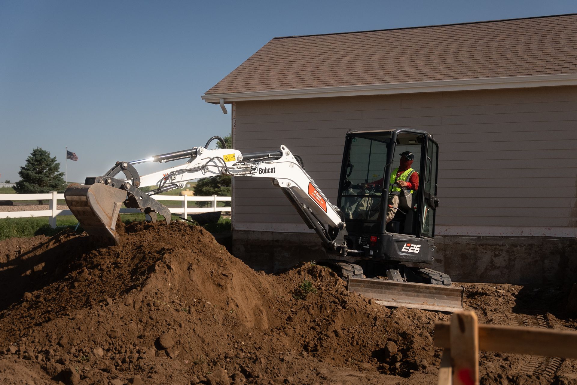 Bobcat excavator digging earth next to a building on a sunny day.
