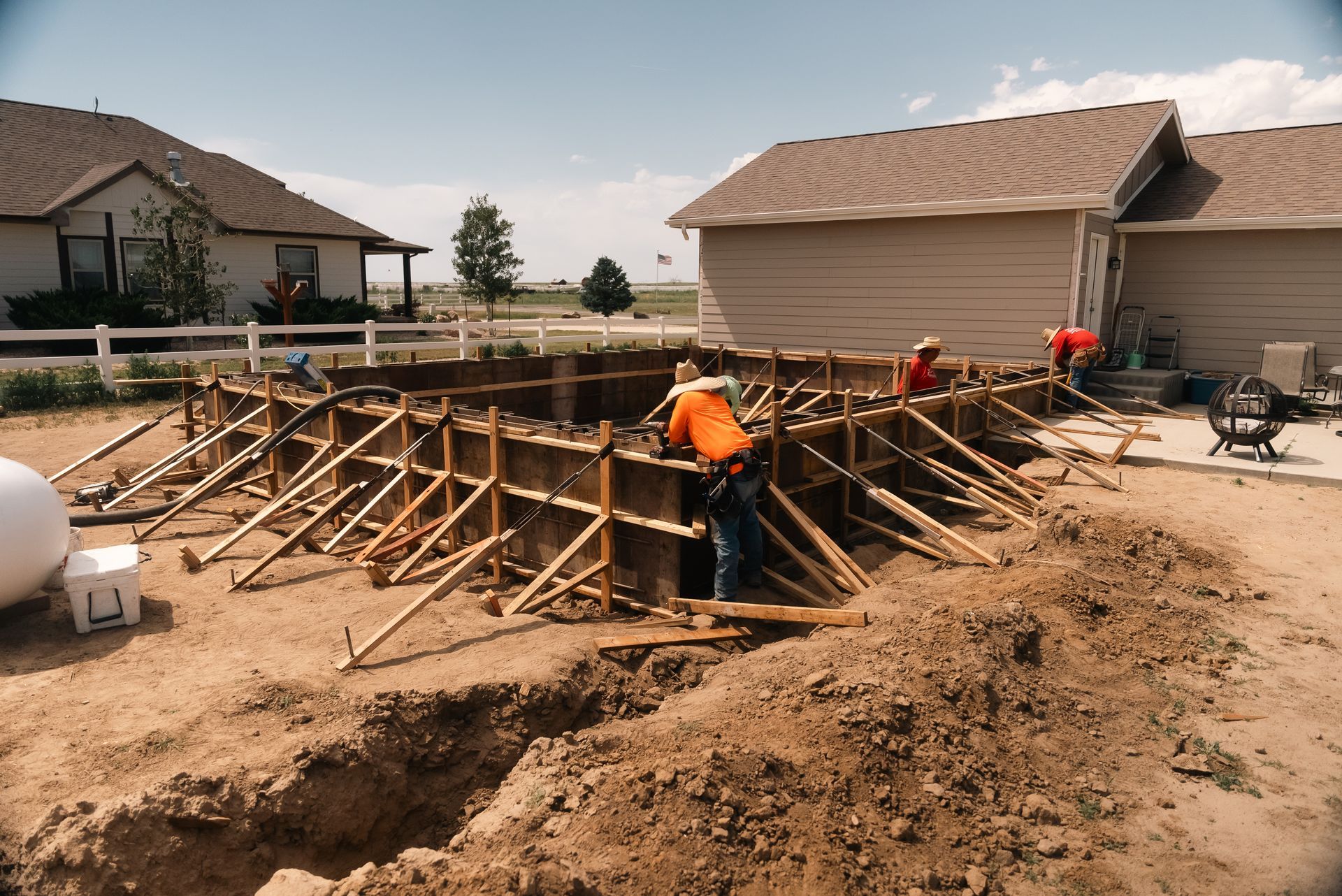 Workers building a concrete structure in a residential yard, with wood forms and bracing.