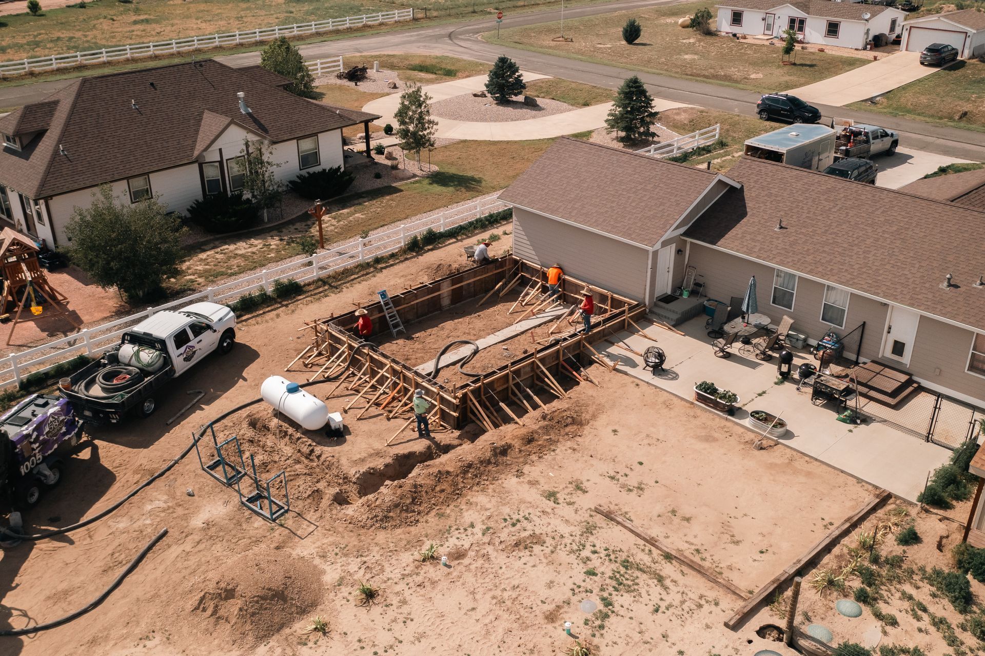 Construction site with workers building a wooden form for a pool in a backyard near houses.