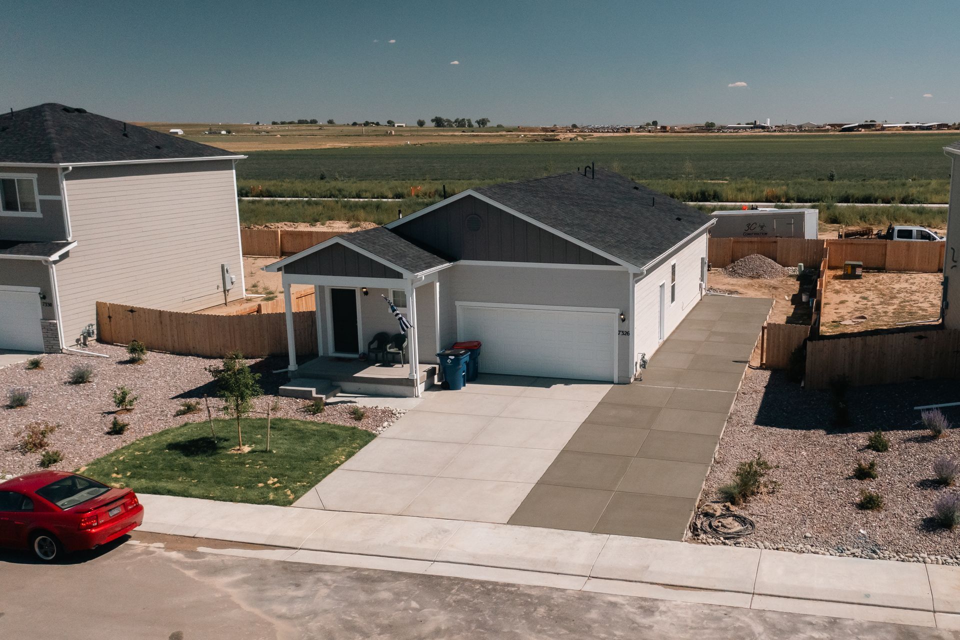 Residential home exterior with red car, blue trash bins, and landscaping.