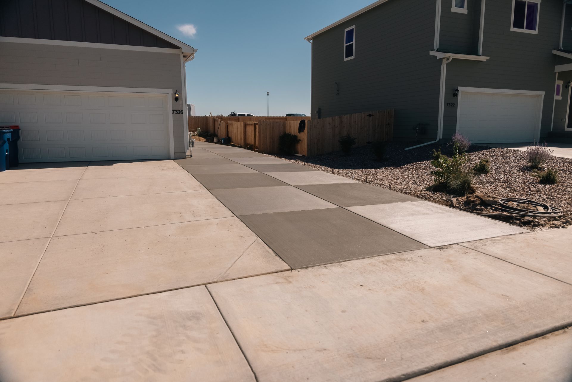 Driveway with concrete and gray paving stones leading to houses, under a blue sky.