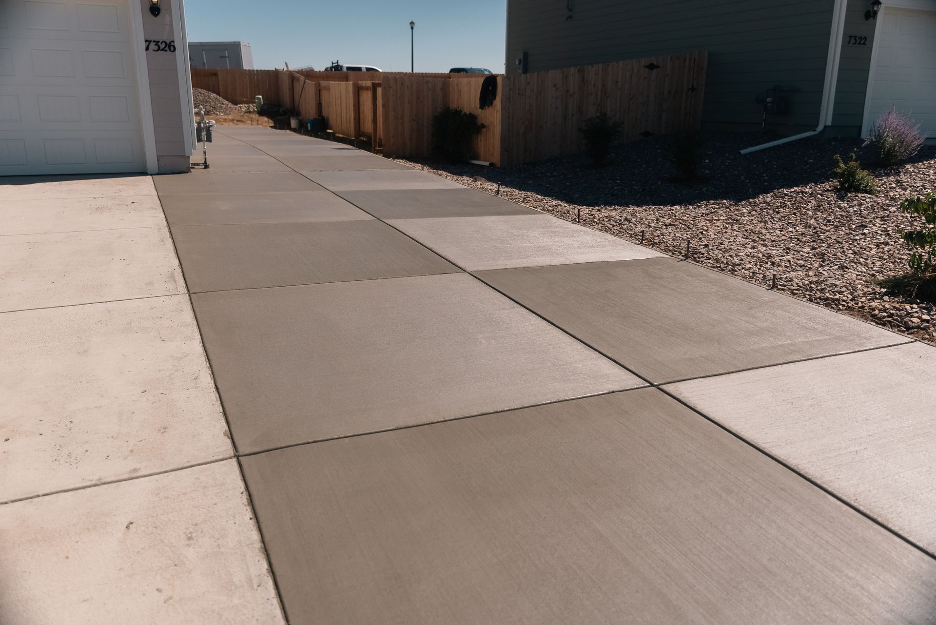 Driveway with square concrete sections, light and dark grey. Houses and a fence are in the background.