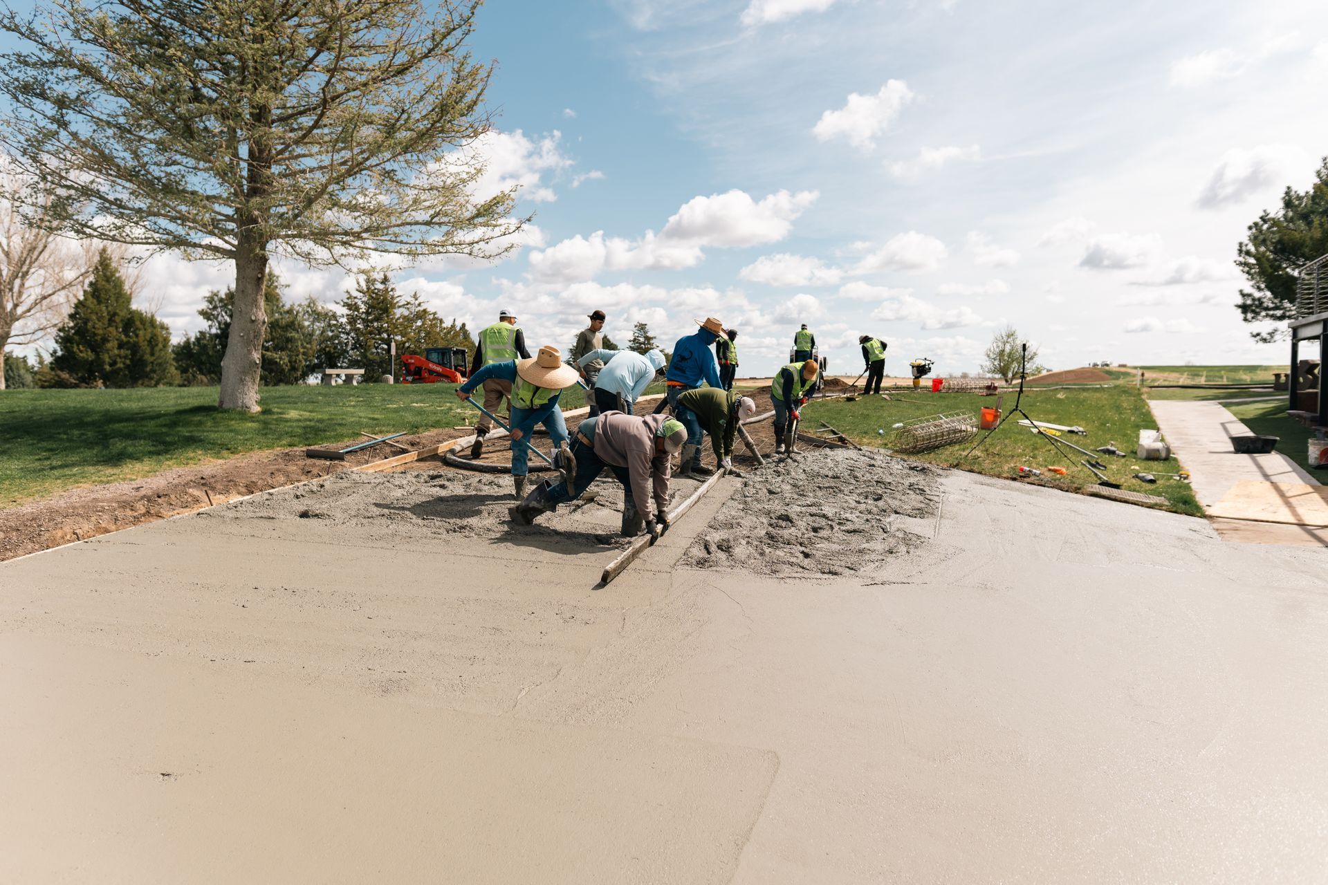 Construction workers pouring and smoothing wet concrete on a road under a blue sky.