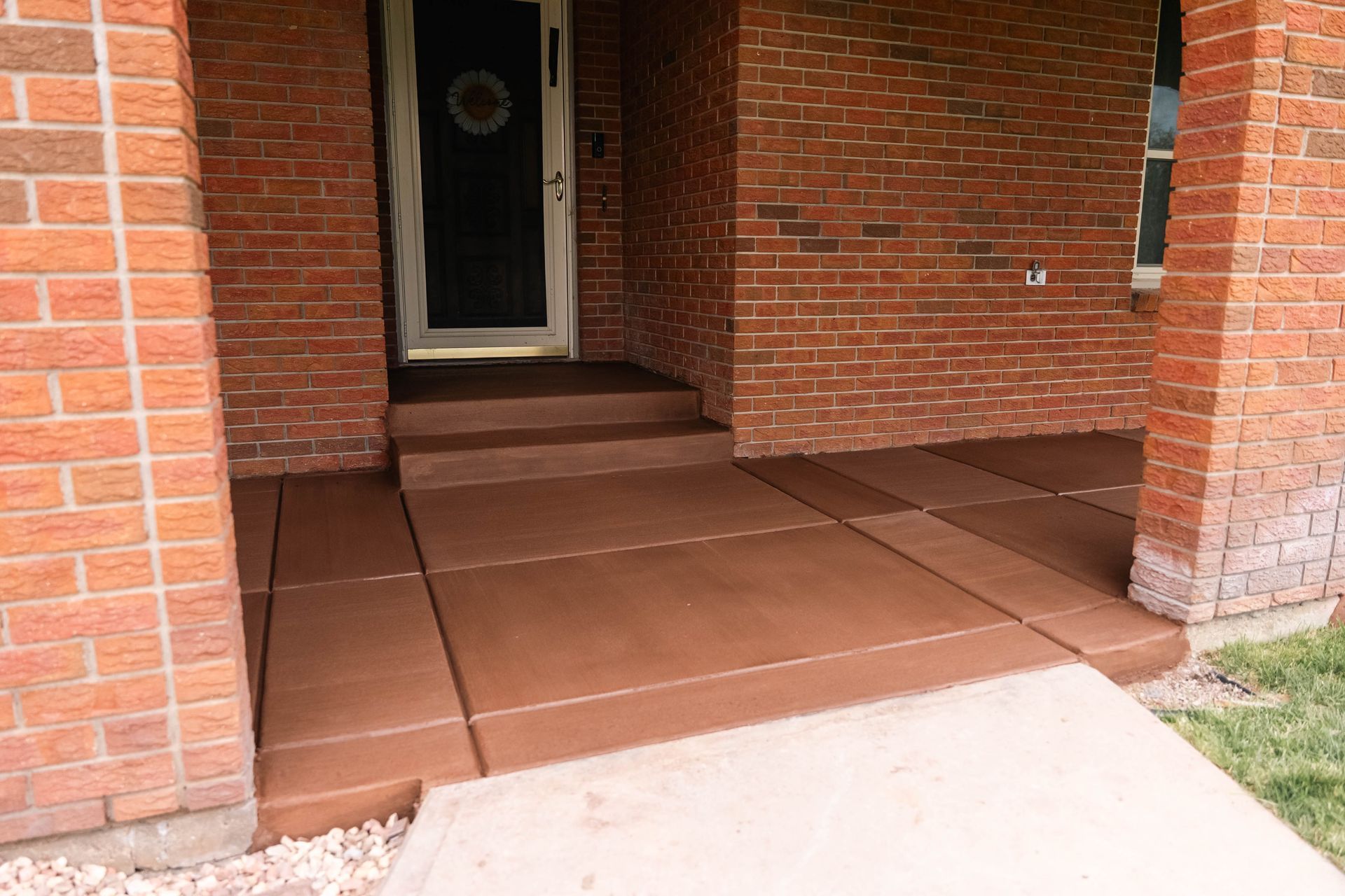 Brown concrete porch with steps, brick walls, and a front door.