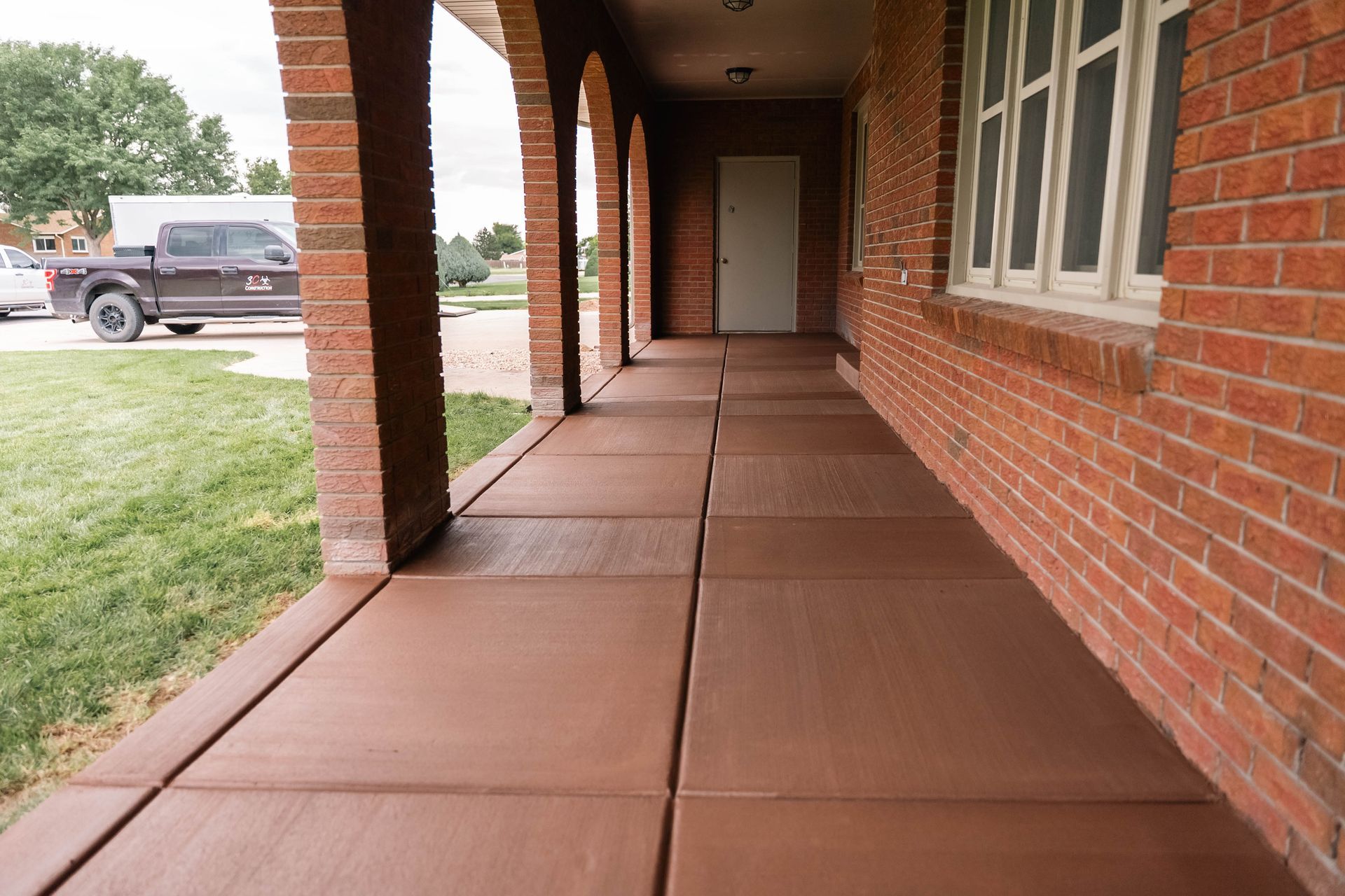 Brown concrete walkway with brick pillars and a red brick wall.