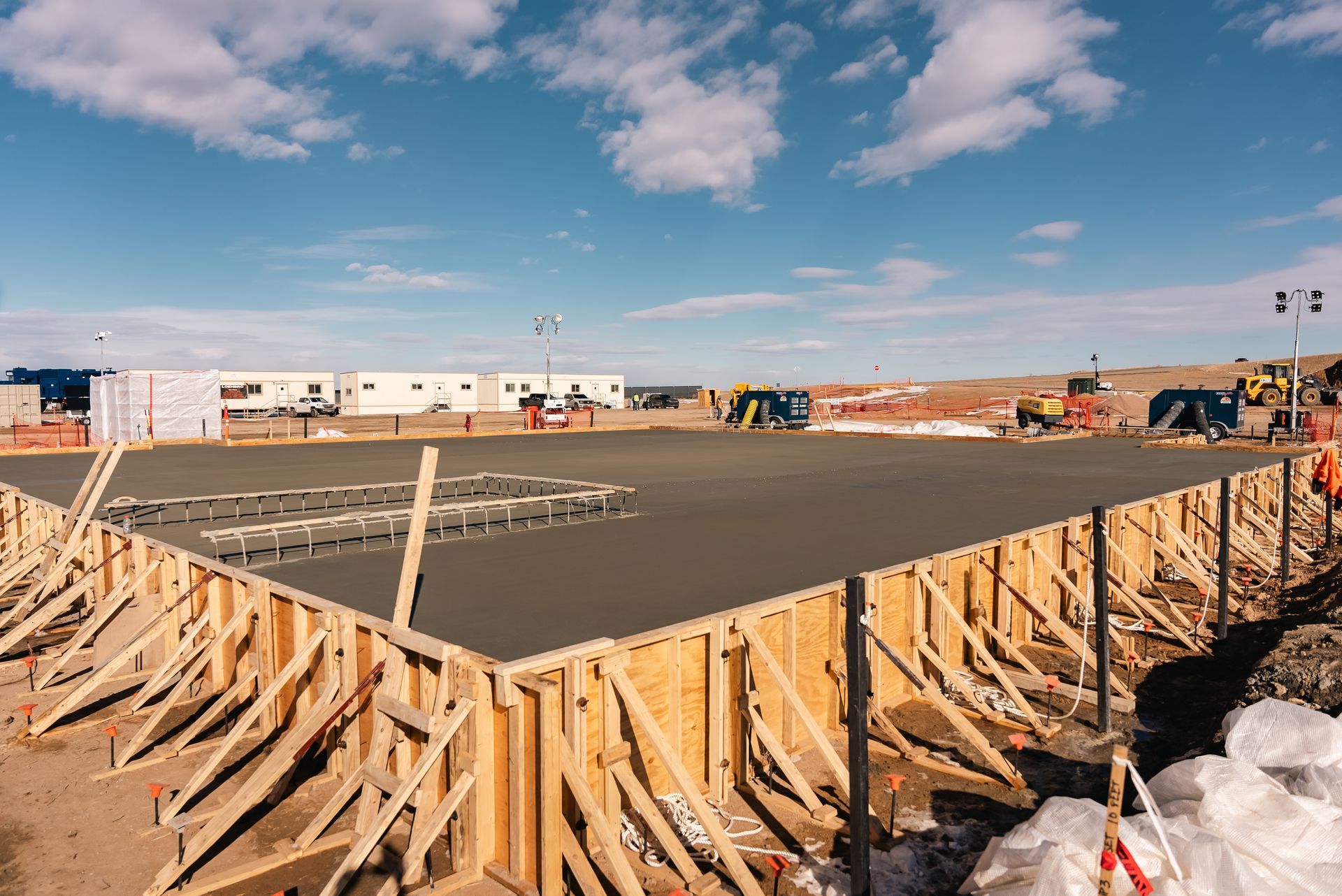 Freshly poured concrete foundation within wooden forms on a construction site; blue sky.