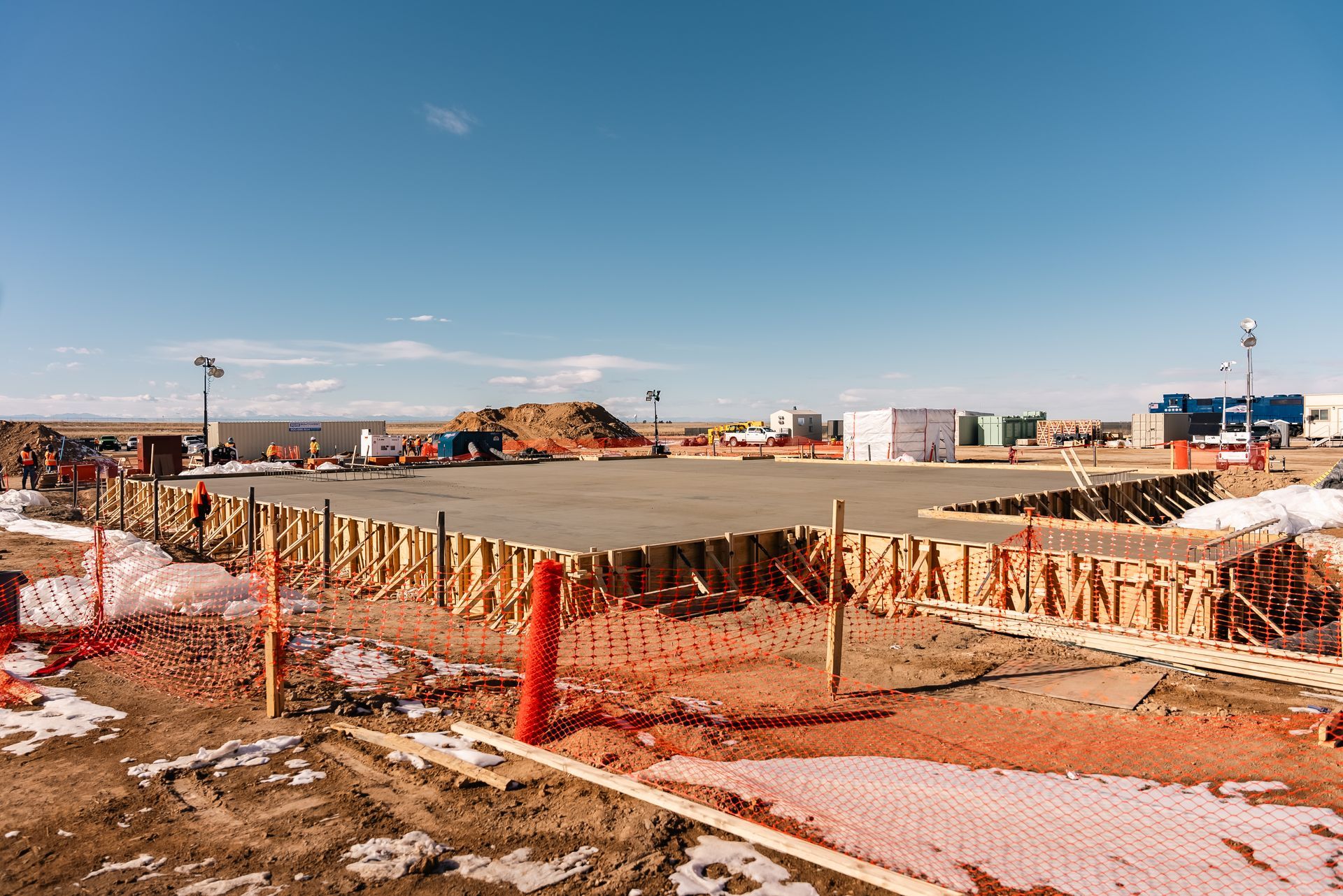 Construction site with wooden forms and concrete slab under a blue sky.