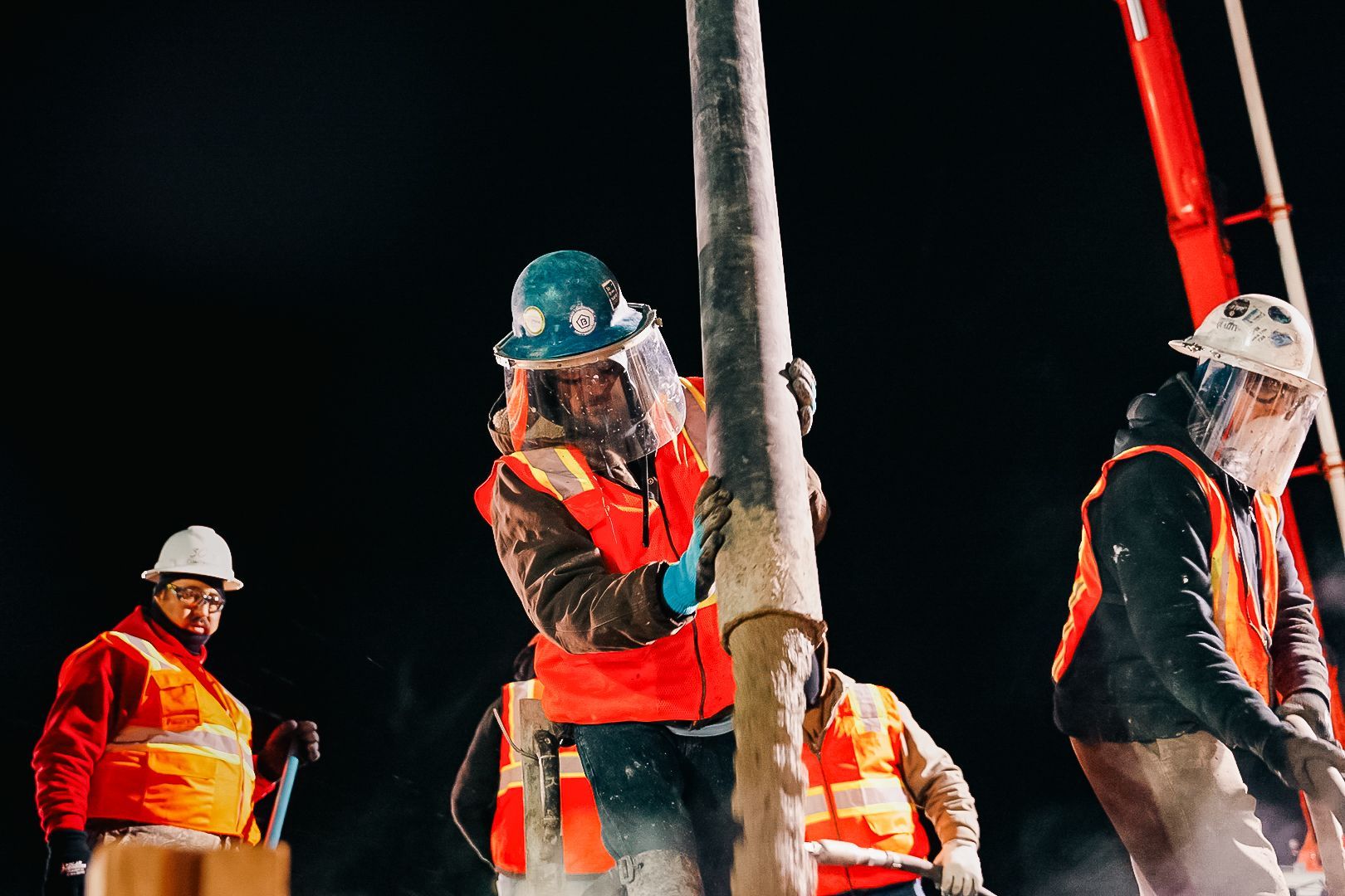 Construction workers in safety vests and hard hats work at night with a large pipe.
