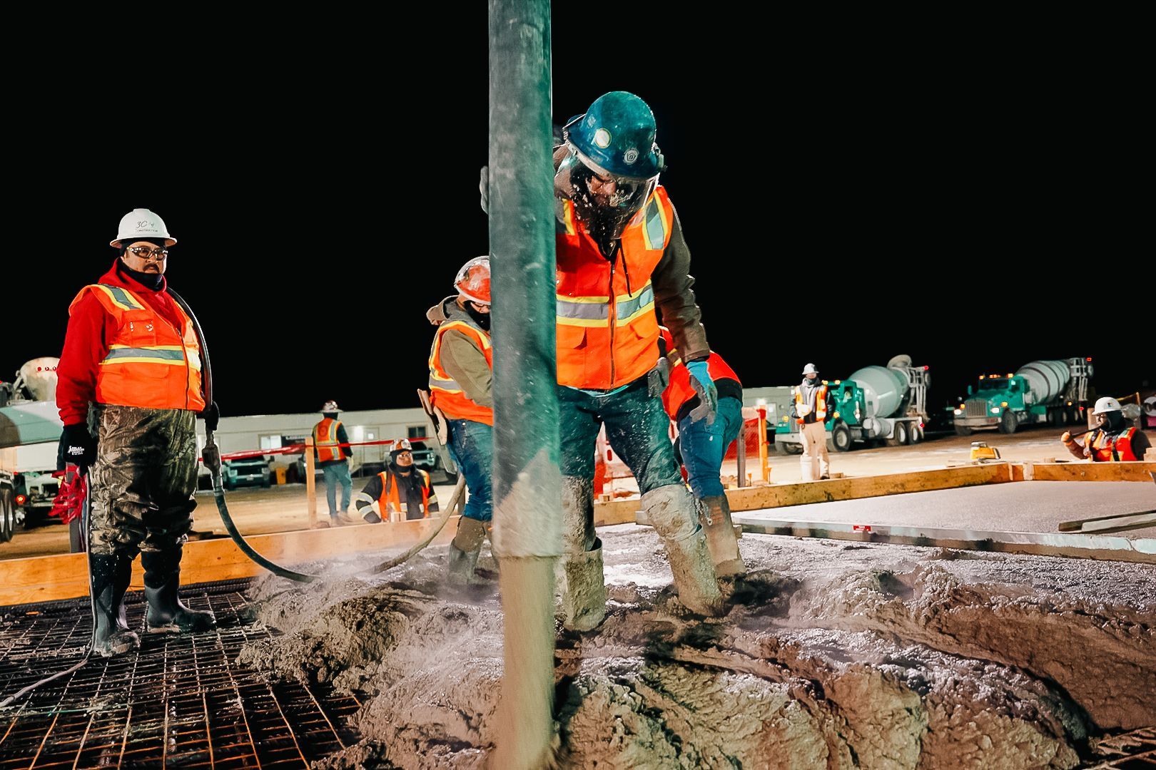 Construction workers pouring concrete at night. Workers wear safety vests, helmets, and work boots.