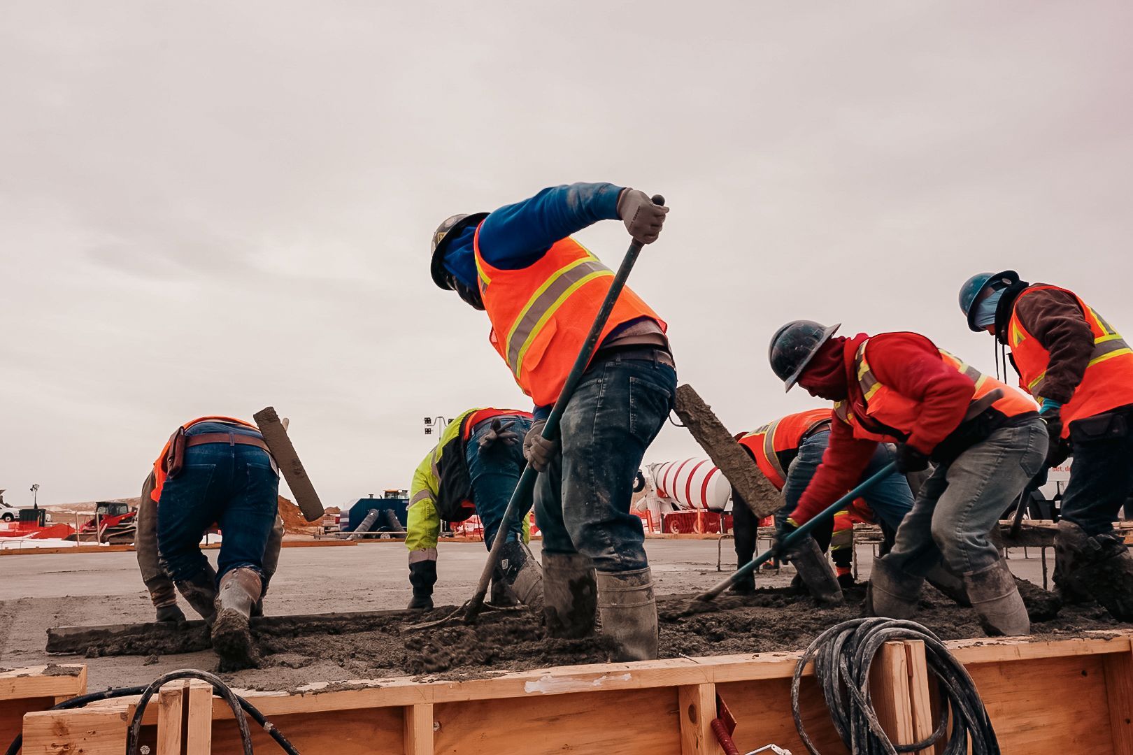 Construction workers in safety vests, shoveling and smoothing wet concrete on a worksite.