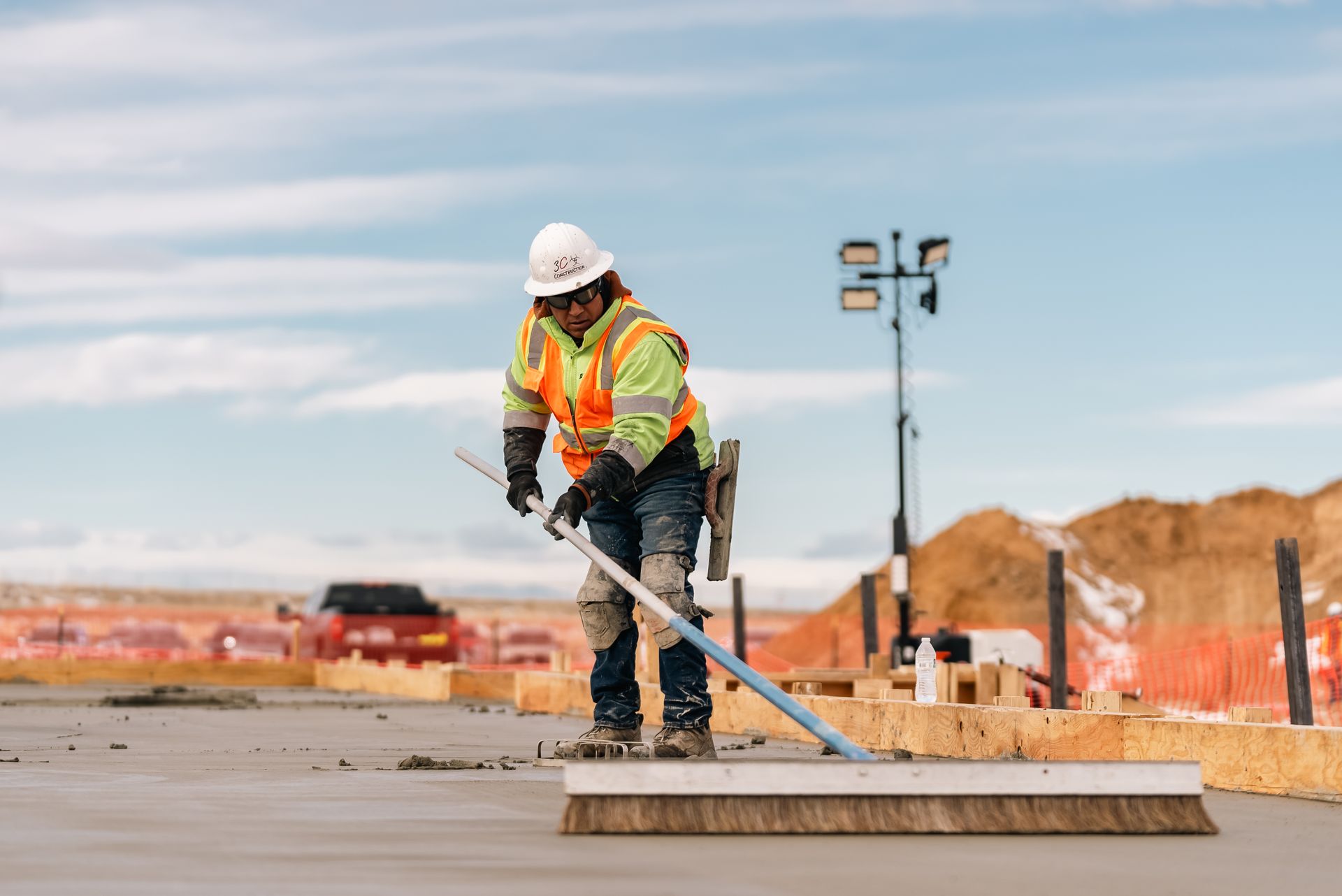 Construction worker smoothing concrete with a broom on a sunny day.