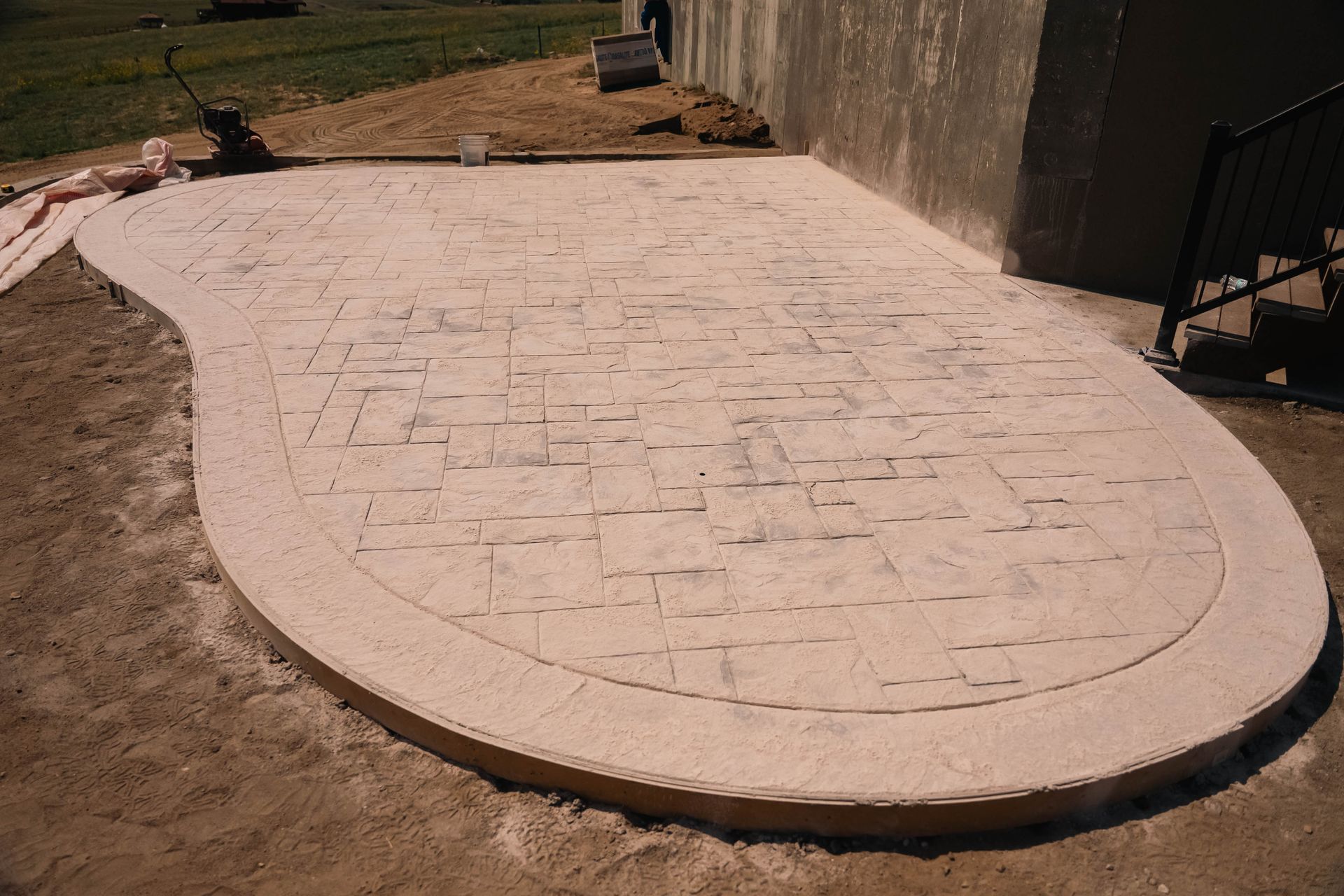 Concrete patio with brick pattern and rounded border against a wall.