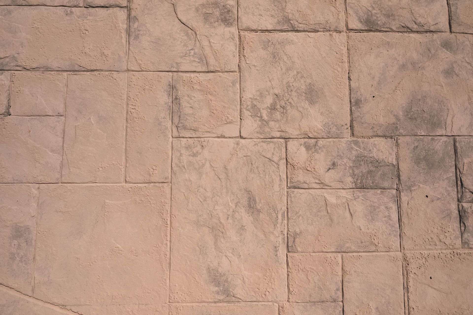 Textured, light brown concrete pavement with rectangular and square tile patterns.