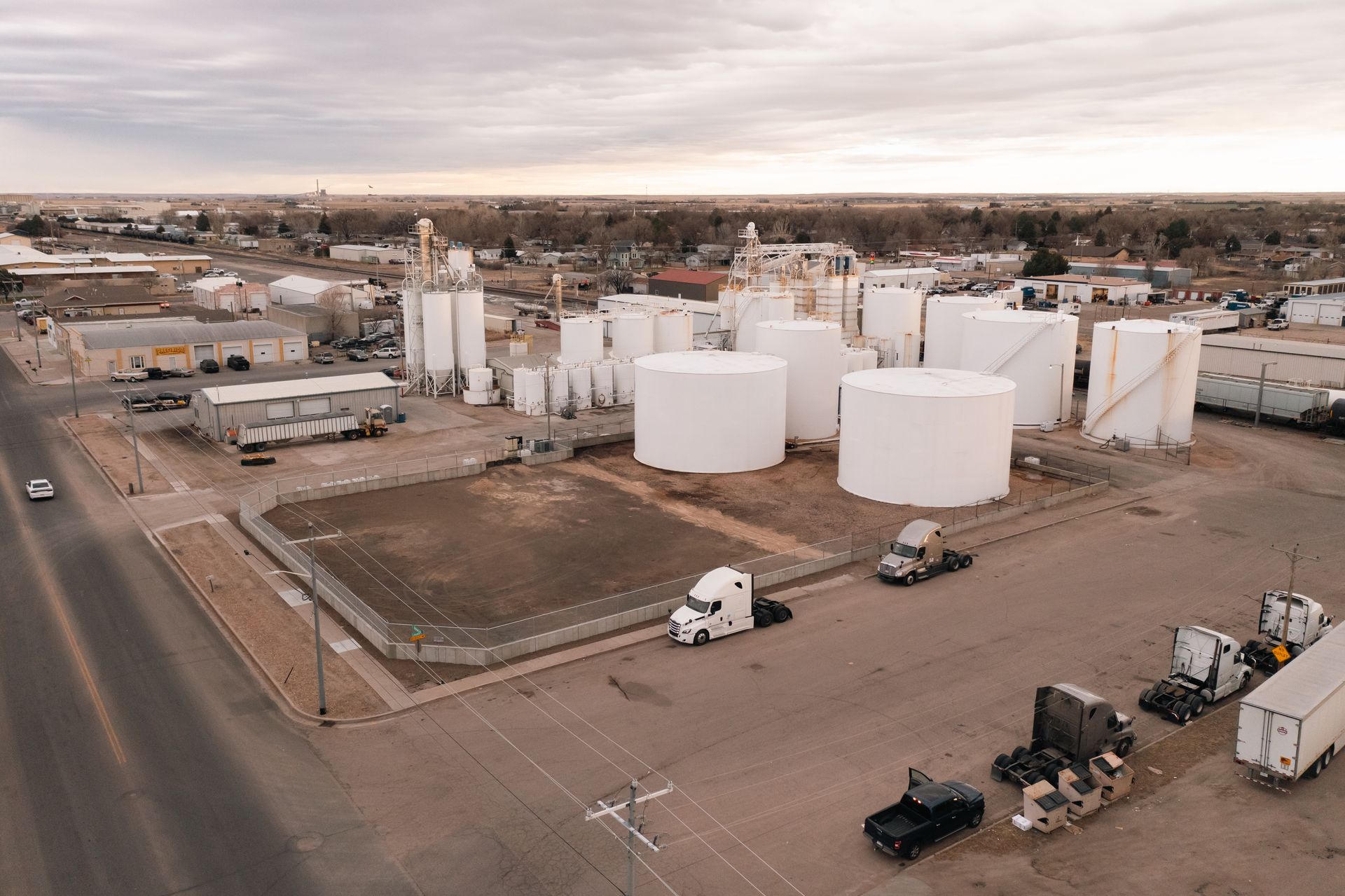 Aerial view of an industrial facility with large white storage tanks and several semi-trucks parked nearby.