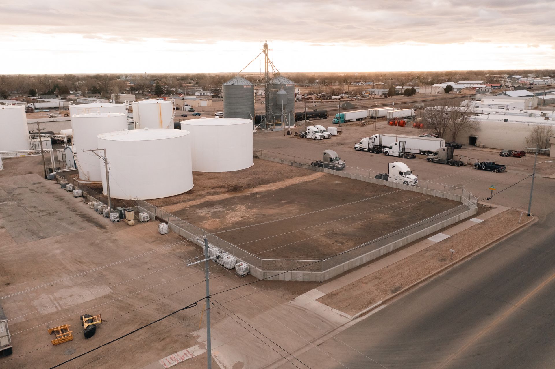 Aerial view of an industrial site with white storage tanks, grain silos, trucks, and a concrete containment area.