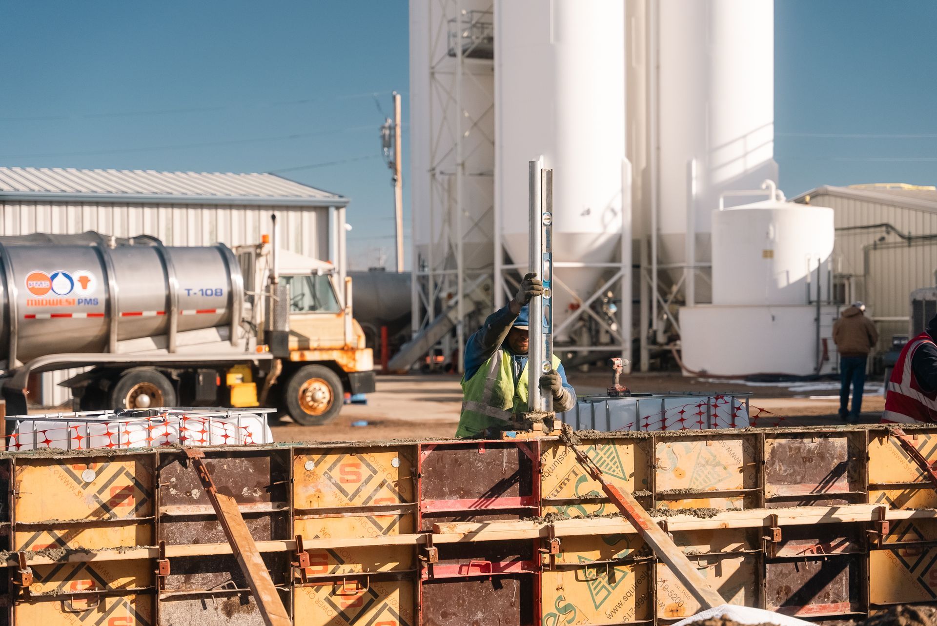 Construction workers at site with concrete trucks and silos, prepping for pour.