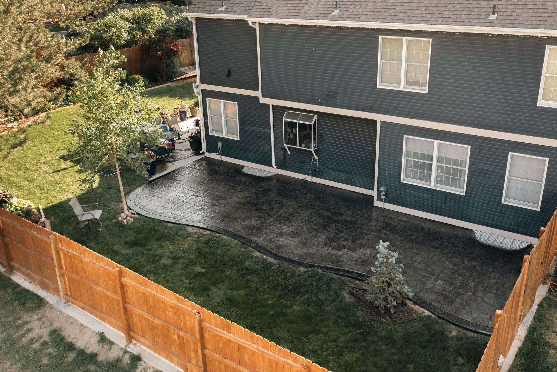 Backyard with dark blue house, wooden fence, patio, and green lawn.