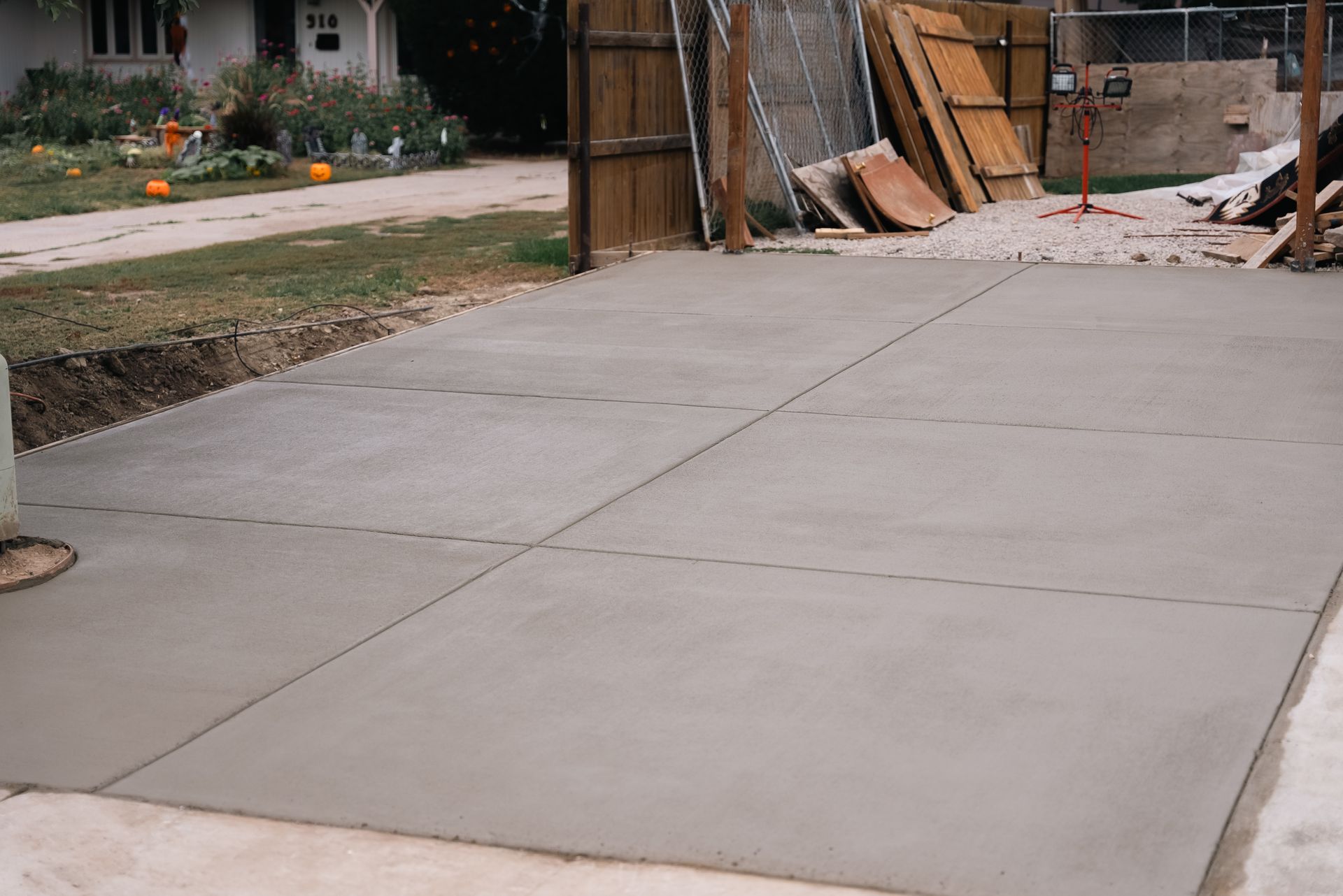 Newly poured concrete driveway with saw cuts, leading towards a wooden fence and house.