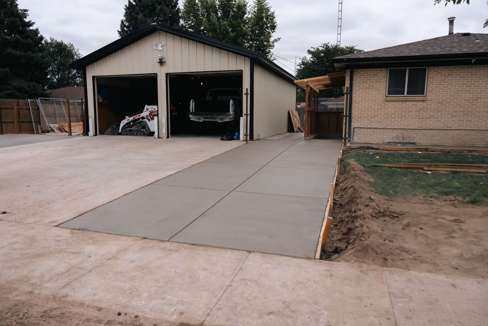 New concrete driveway leading to a garage with open doors. The house is on the right side.