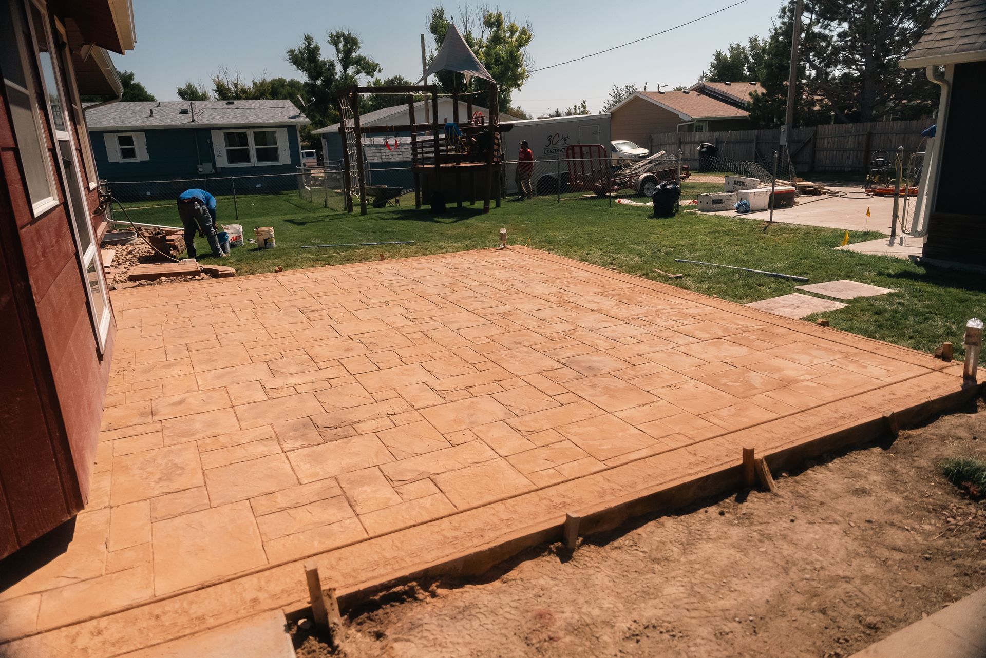 Finished brick patio in a backyard with a house on the left, other houses in the background.