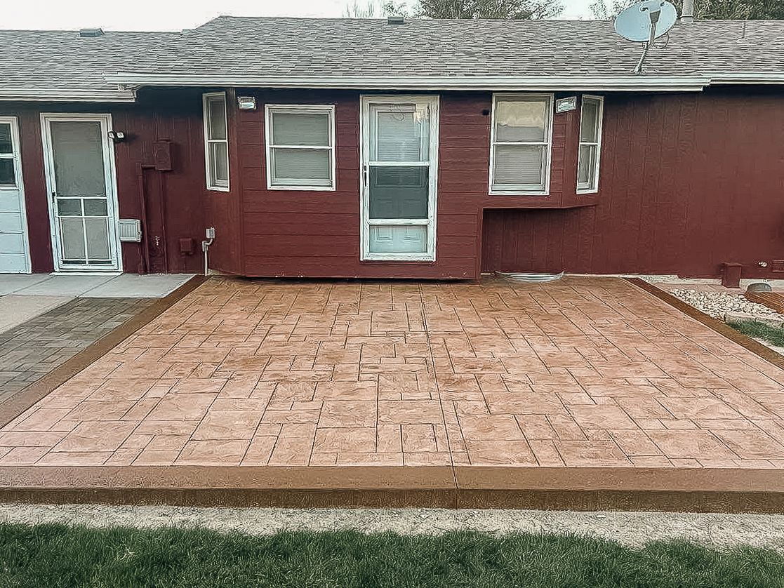 Backyard patio with stamped concrete, brown border, and red house.