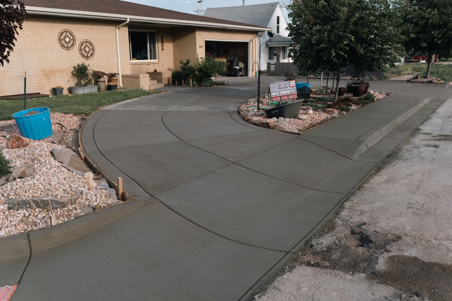 New concrete driveway curves in front of a tan house with a partially visible garage.