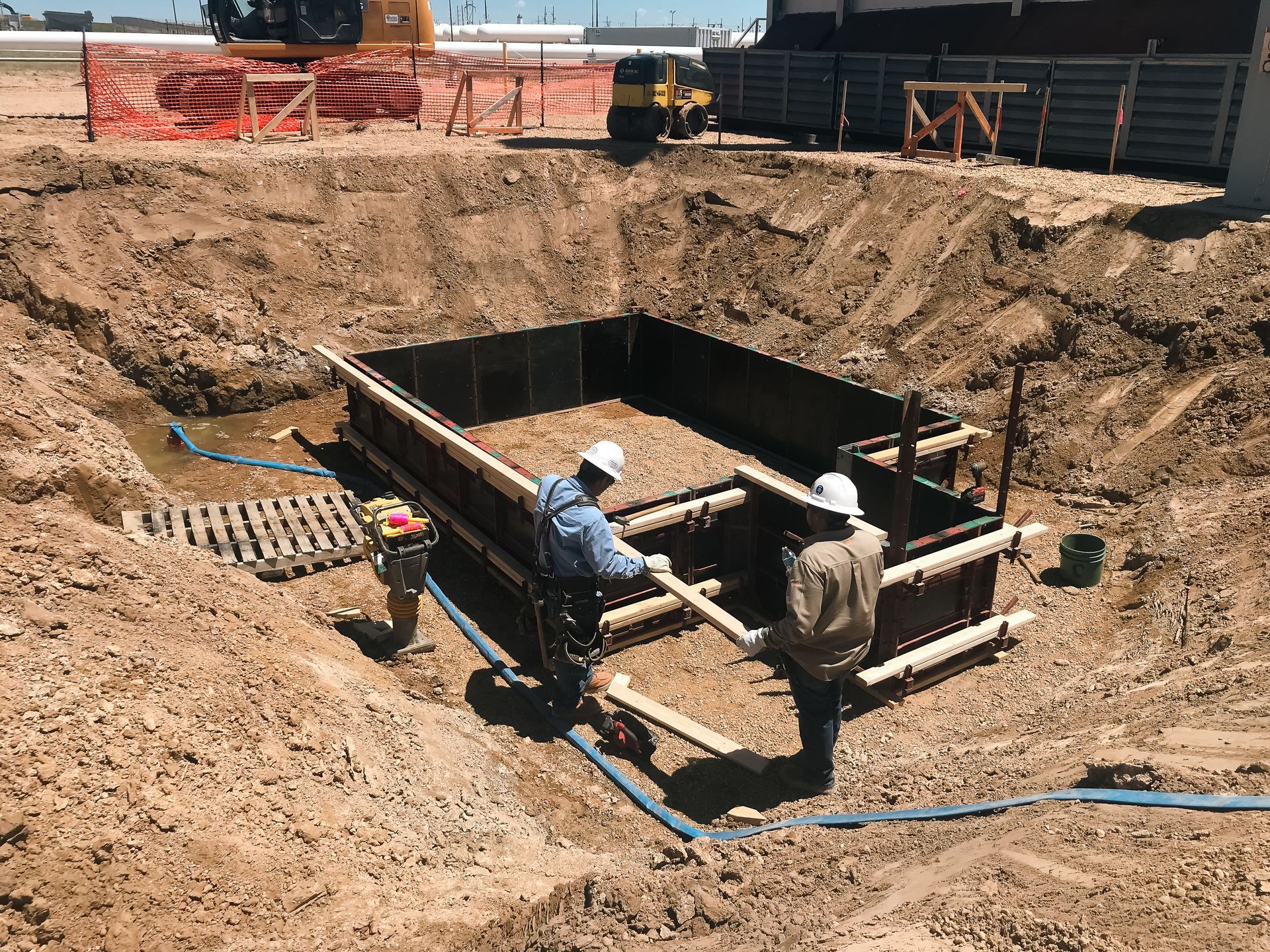 Two construction workers are working on a large hole in the ground.