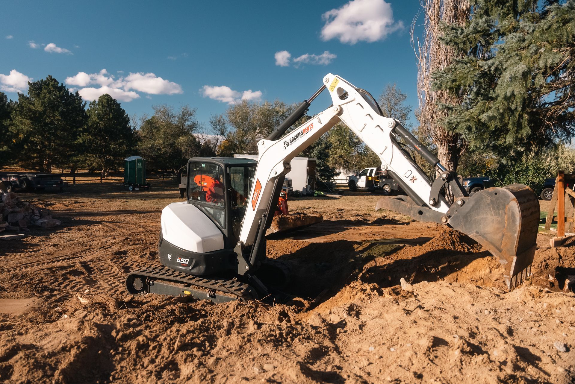 White Bobcat excavator digging in a dirt area, blue sky in the background.