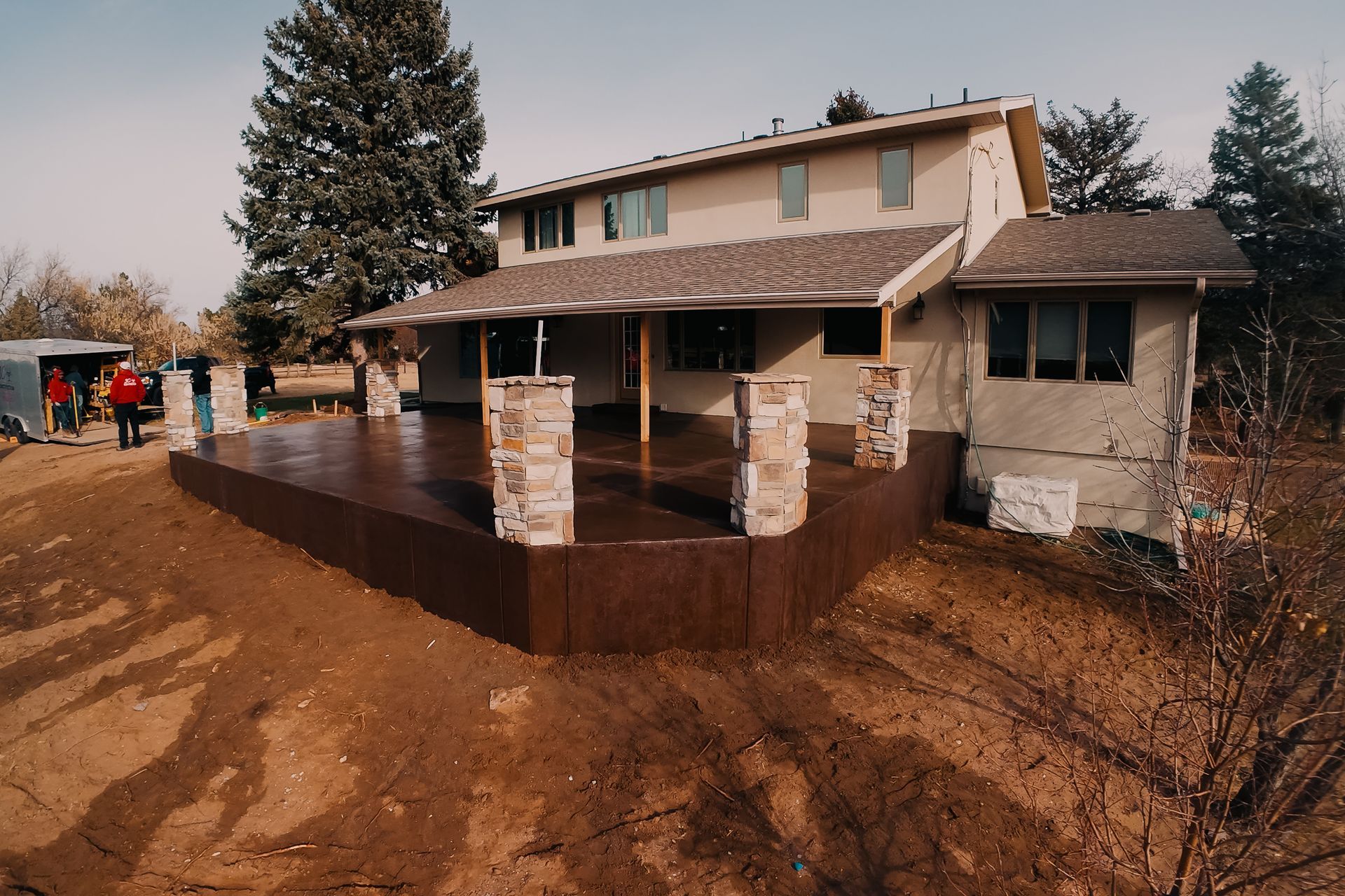 A two-story house with a newly built brown deck; workers stand near a red shed on a fall day.