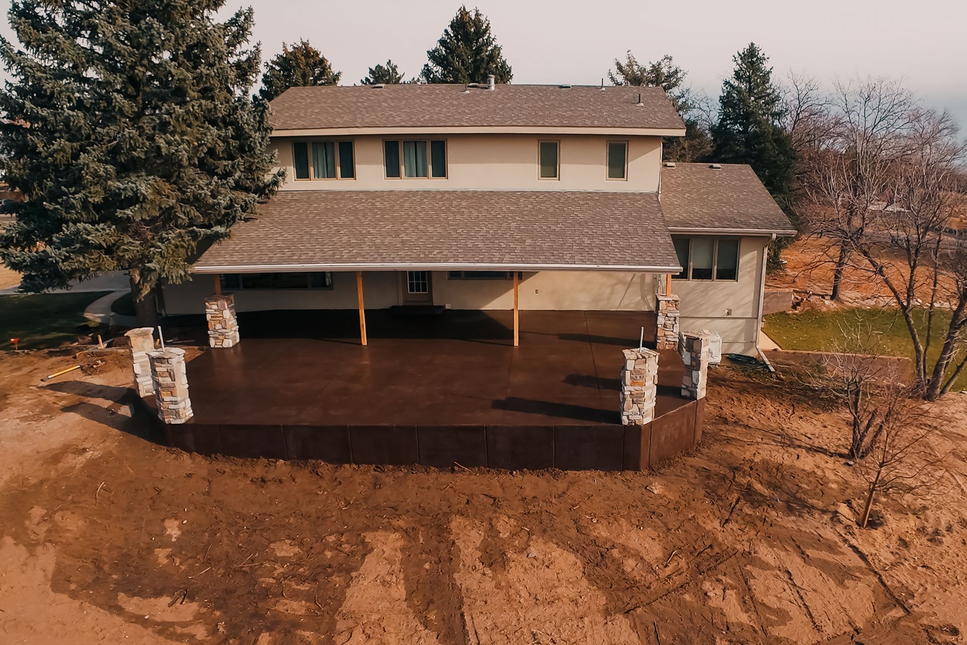 Two-story house with a large brown deck. Stone pillars support the deck's roof.