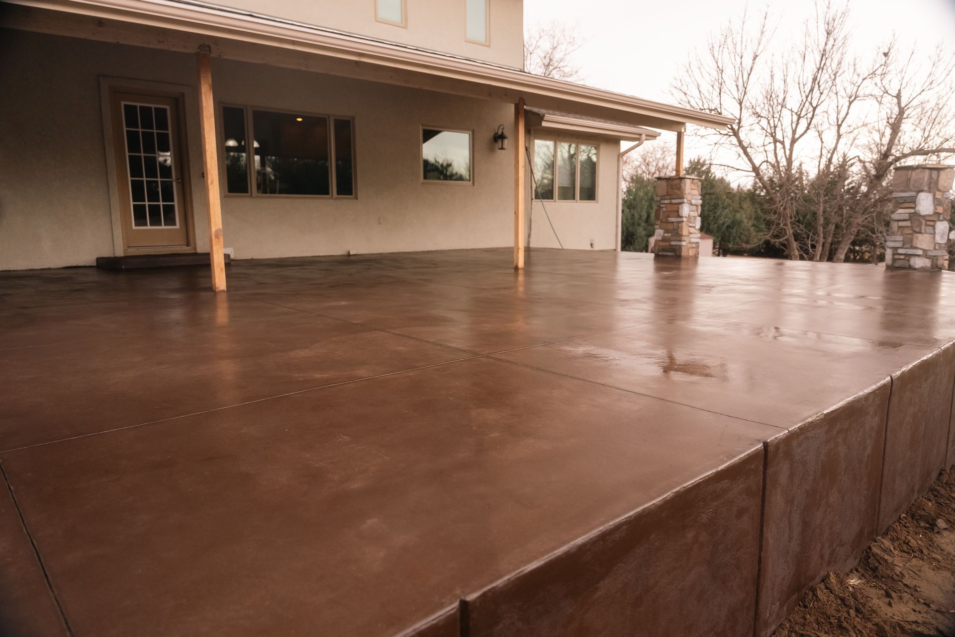 Brown concrete patio extending from a light-colored building, with columns and windows visible.