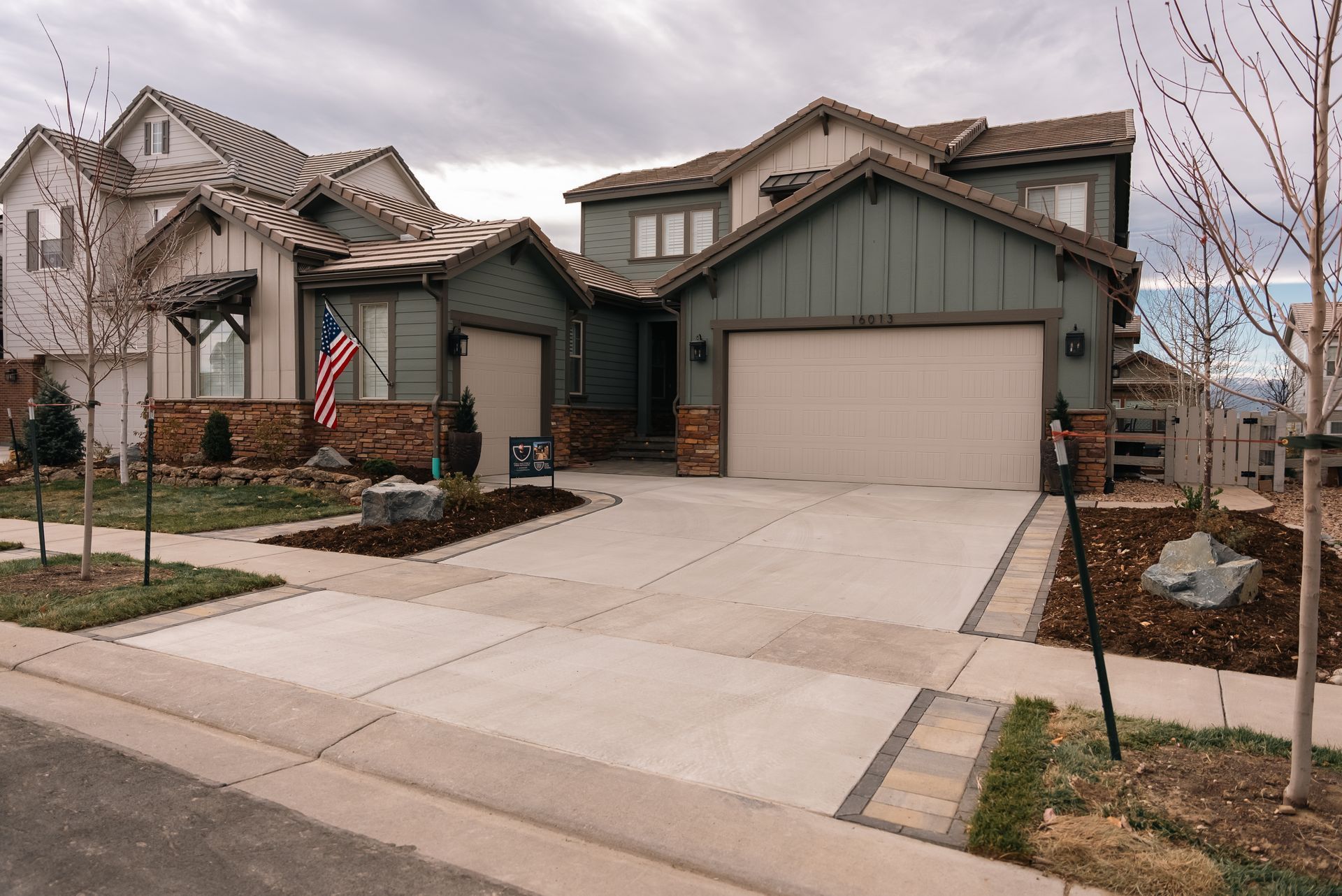 A two-story house with a green exterior, attached garage, and American flag; cloudy day.