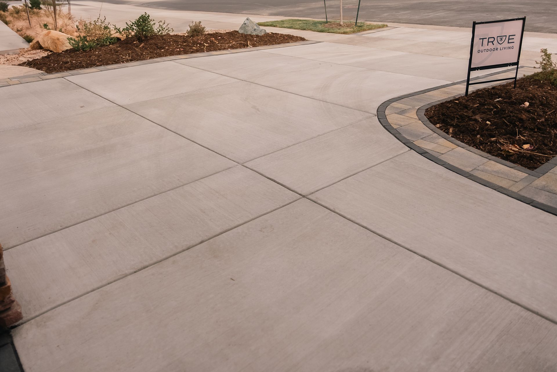 Concrete driveway with cross joints, brown mulch beds, and a sign.