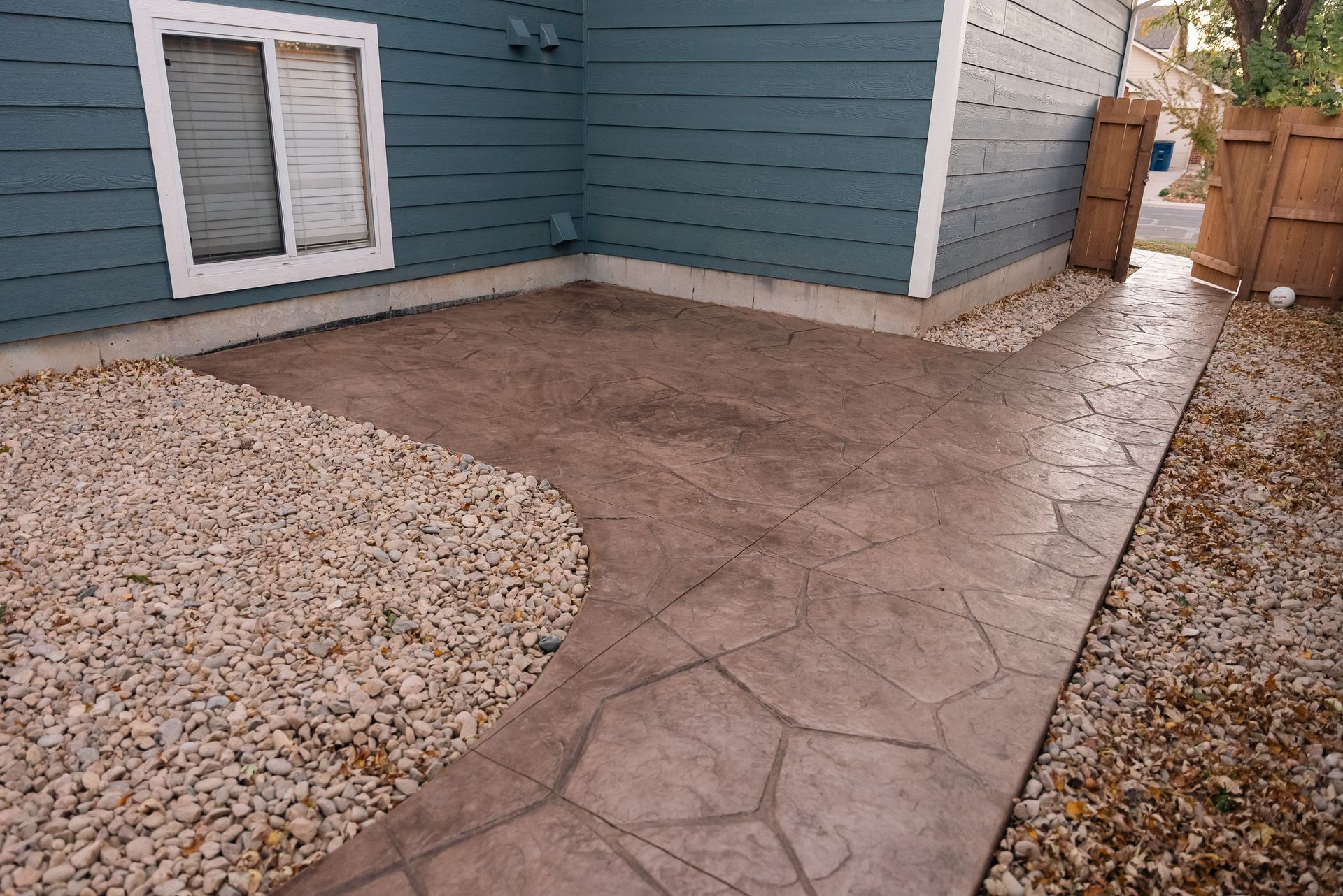Concrete patio and walkway with a stone texture next to a blue house and gravel.